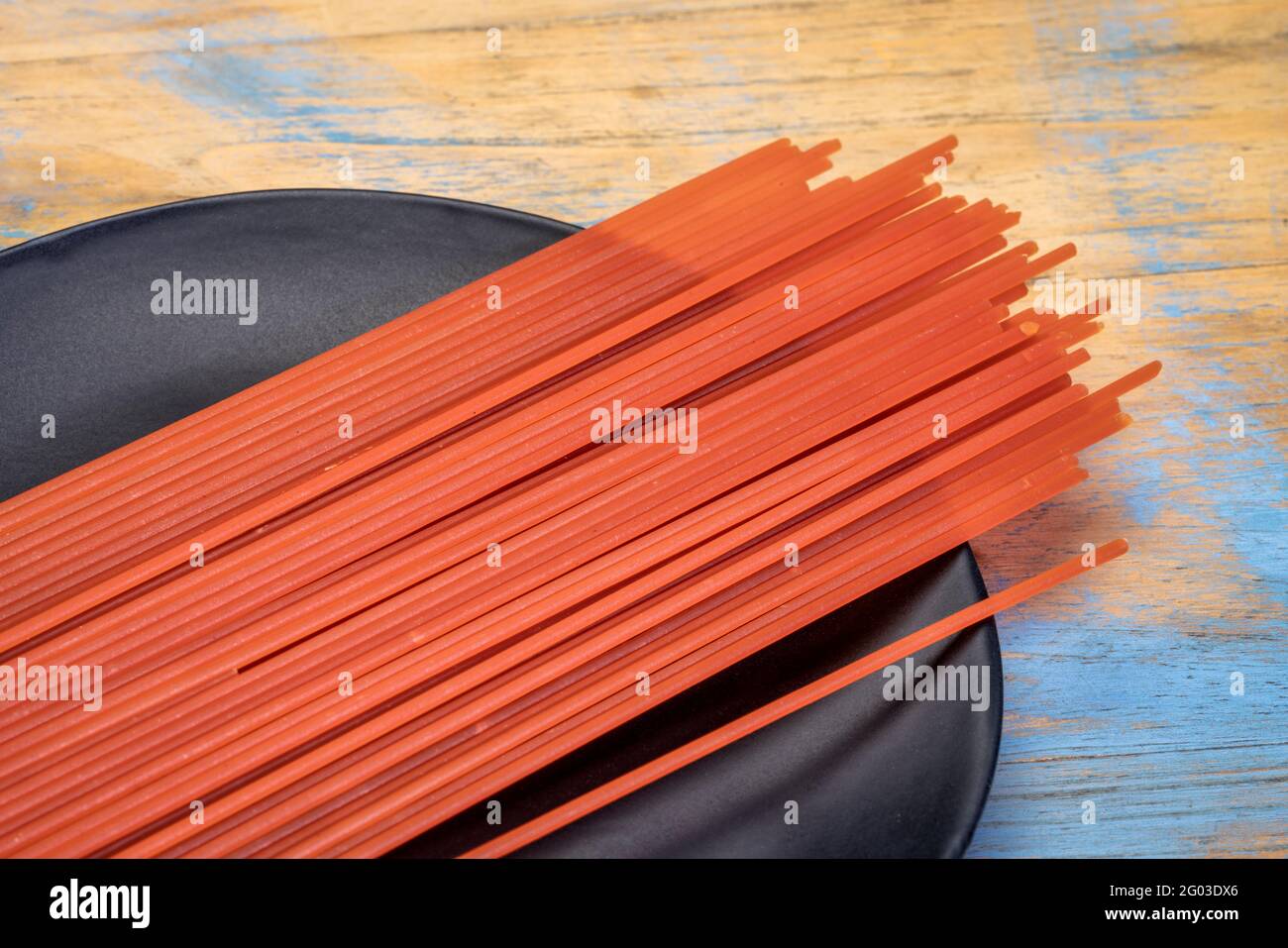 Pasta italiana di spaghetti senza glutine e cereali, proveniente da farina di lenticchie rosse, piastra nera contro legno rustico Foto Stock