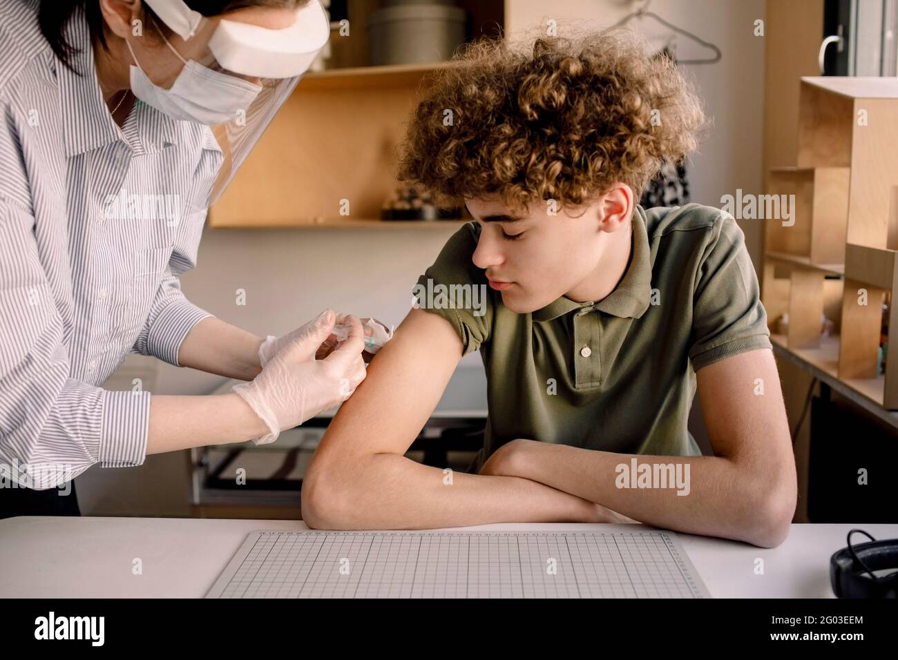 Ragazzo con capelli castani ricci che guarda l'infermiera che inietta la medicina a casa Foto Stock