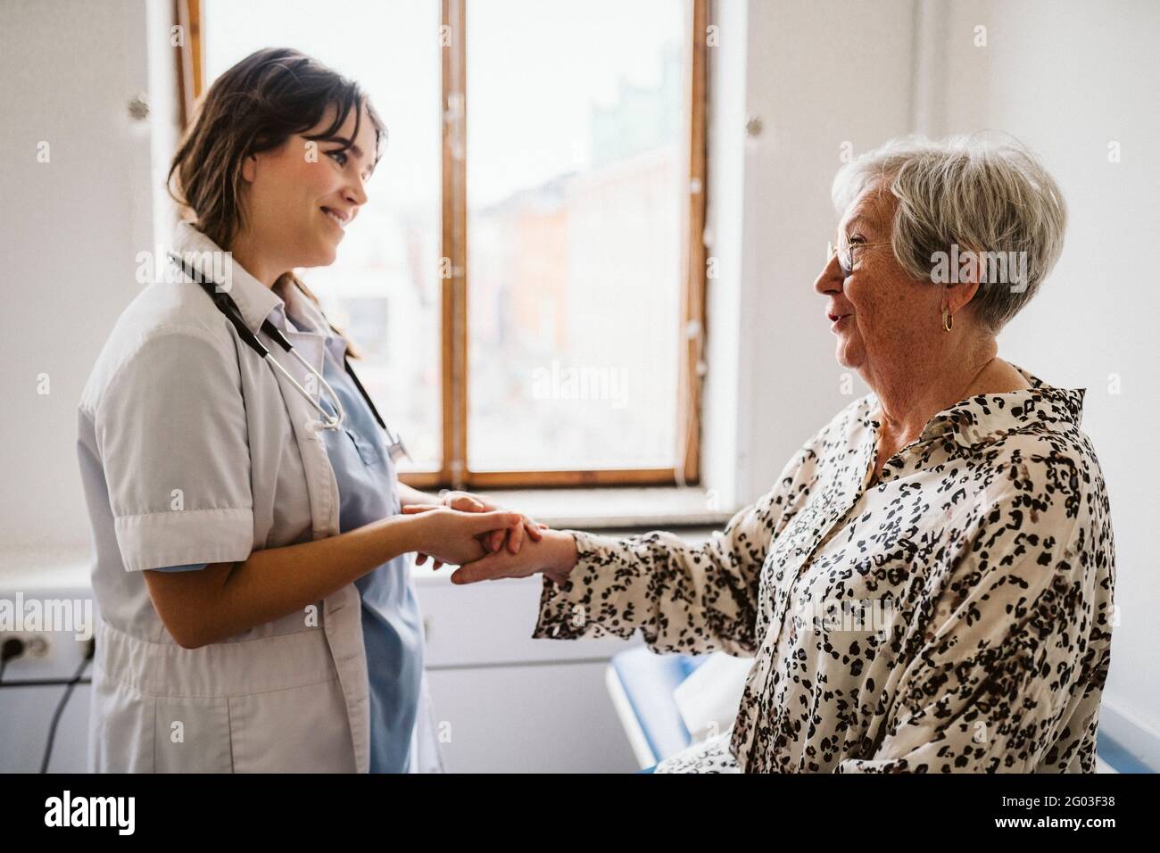 Sorridente operatrice sanitaria che guarda pazienti anziani parlare mentre si tiene le mani Foto Stock