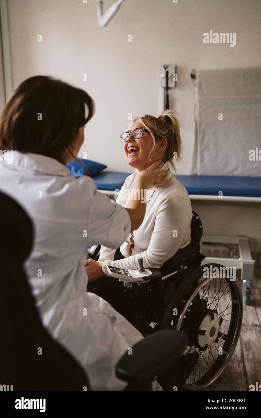 Femmina medico esperto controllo impulso di sorridente donna disabile presso la clinica medica Foto Stock