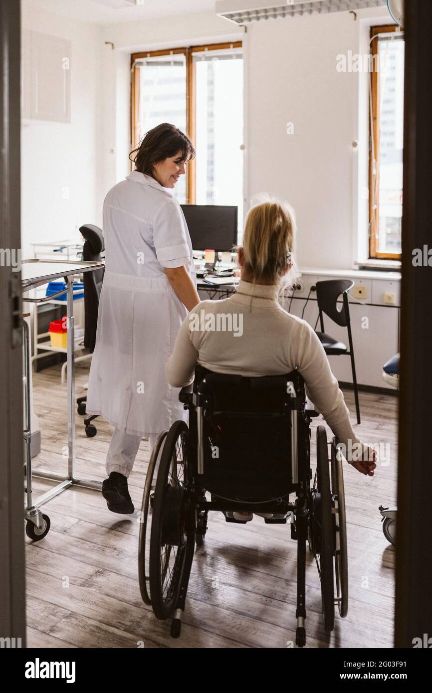 Donna sorridente esperta di medicina che guarda la donna disabile che visita alla clinica medica Foto Stock
