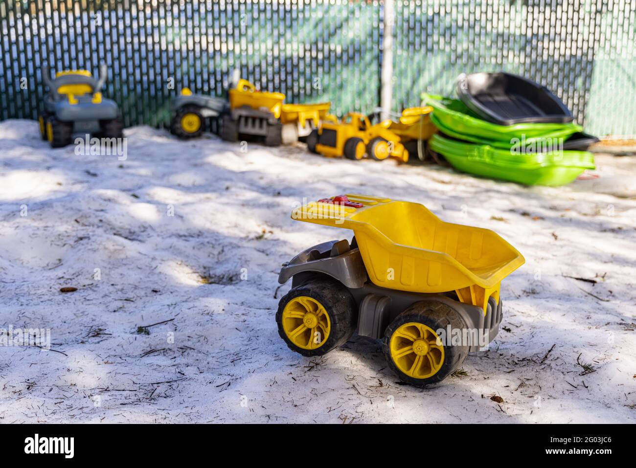 Messa a fuoco selettiva in primo piano. Primo piano di un miscelatore giallo di calcestruzzo nel giardino di un asilo. Altri camion giocattolo e macchinari in sfondo sfocato. Foto Stock
