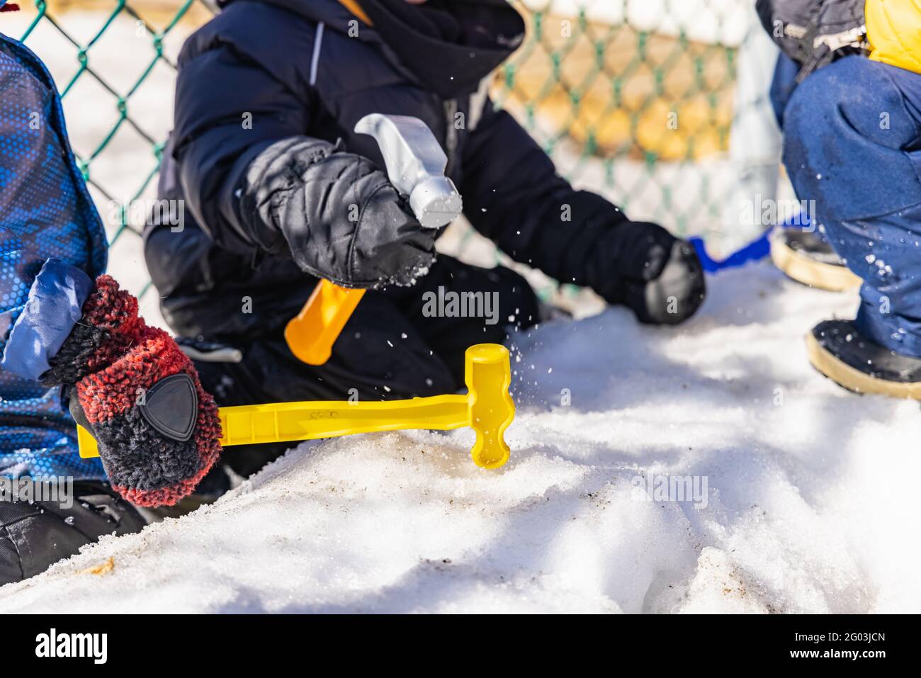 Primo piano di un bambino giovane, non riconoscibile asilo in abiti invernali che gioca nella neve con un martello di plastica giallo. Foto Stock
