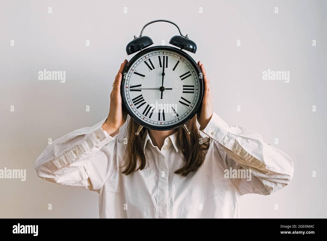 Giovane donna d'affari che ricopre il viso con orologio analogico d'epoca Foto Stock