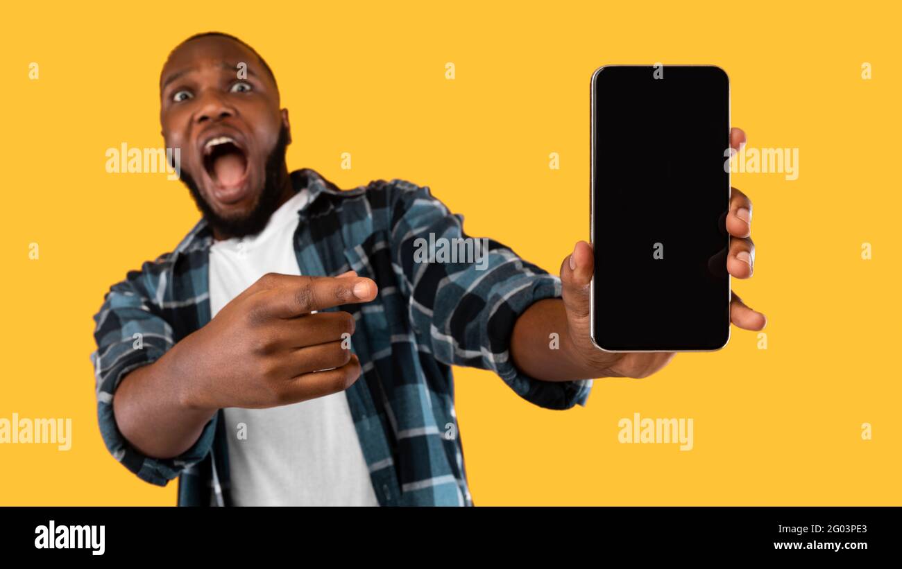 Impressionabile African American Man mostrando schermo del telefono cellulare, sfondo giallo Foto Stock