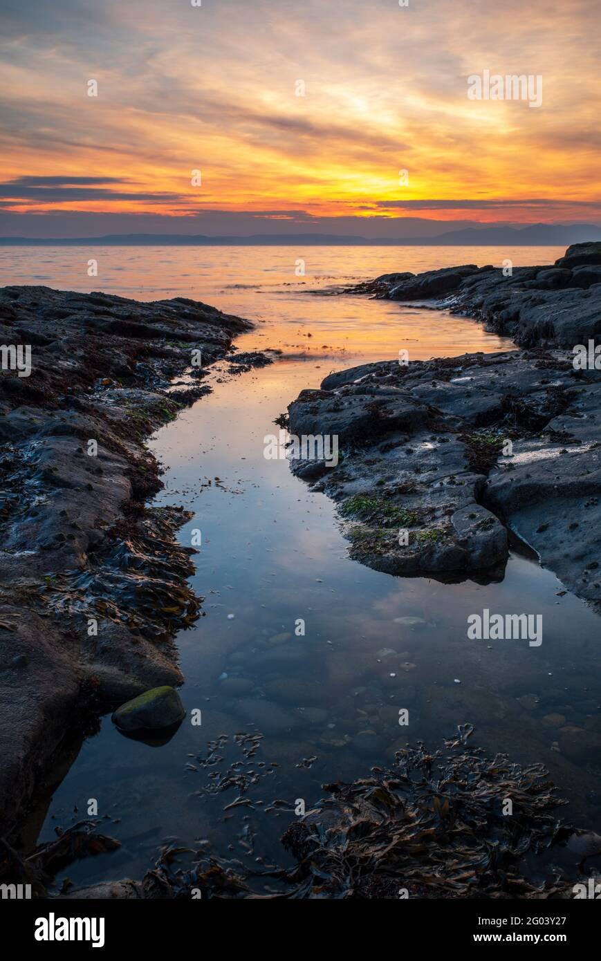 Una splendida vista del tramonto attraverso il Firth di Clyde dalla costa rocciosa lungo la costa dell'Ayrshire a Dunure. Foto Stock