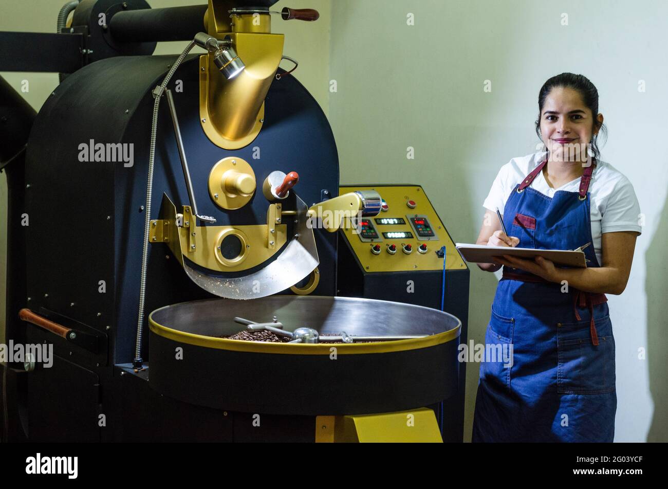 Le mani di una donna tostano i chicchi di caffè aromatici su una moderna macchina utilizzata per tostare i chicchi. Foto Stock