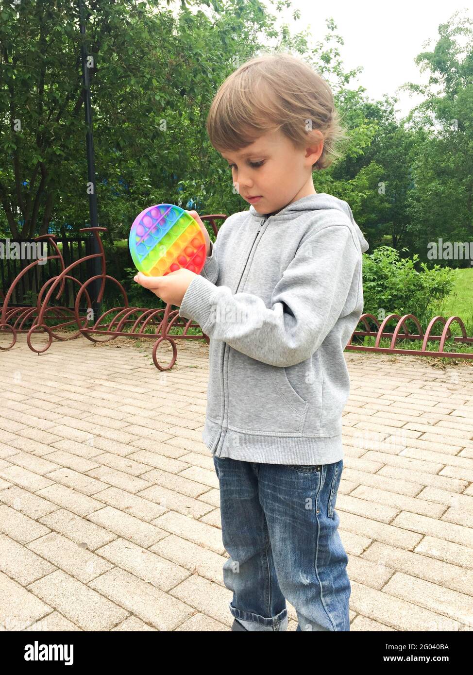 i giocattoli sensoriali anti-stress lo schioccano nelle mani dei bambini. un bambino piccolo e felice gioca con un semplice giocattolo a forma di fossato sulla strada della città Foto Stock