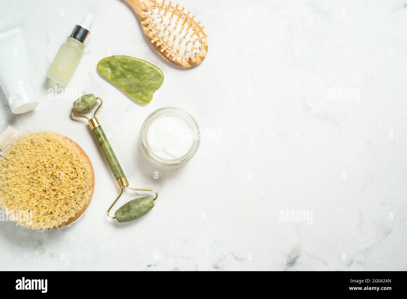 Massaggiatore Jade Roller e pietra gua sha con crema per il viso e bottiglia di siero. Foto Stock