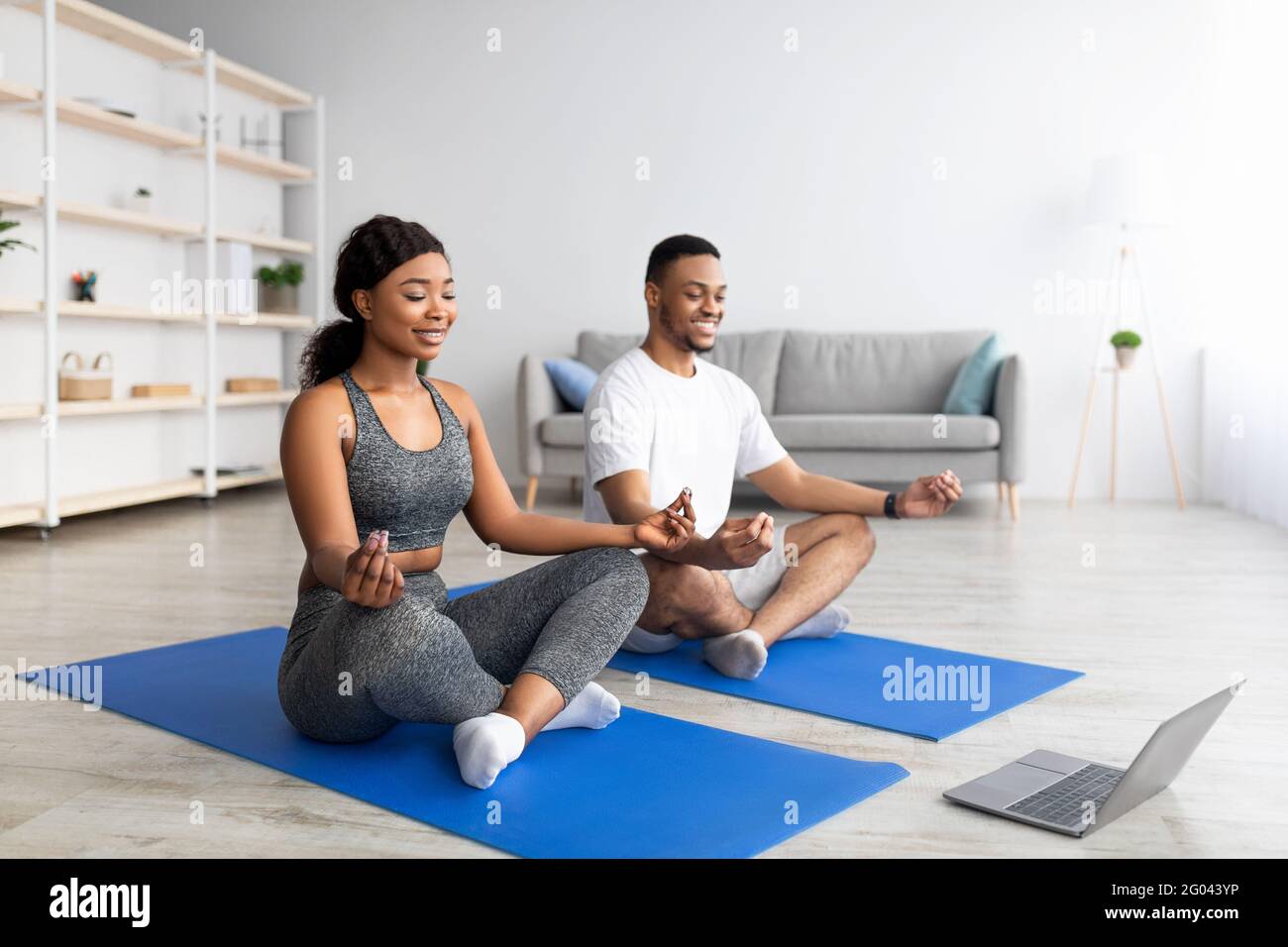 Felice coppia nera che pratica yoga vicino al computer portatile, guardando video tutorial online, meditando o facendo esercizi di respirazione Foto Stock