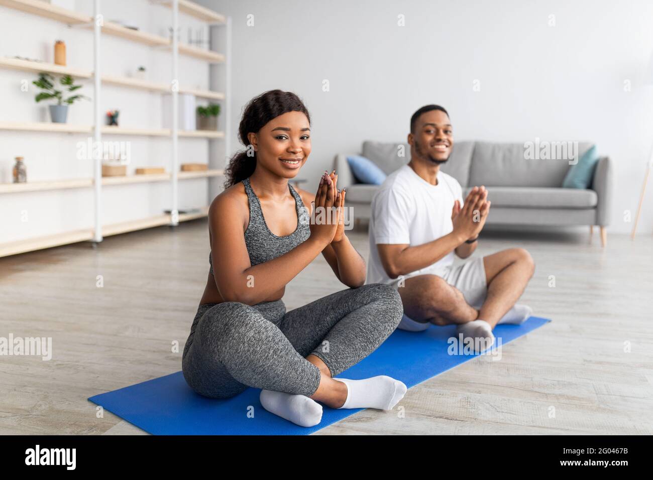 Pratica di yoga domestico durante il covid. Coppia nera meditando o facendo esercizi respiratori, seduto in posa lotus a casa Foto Stock