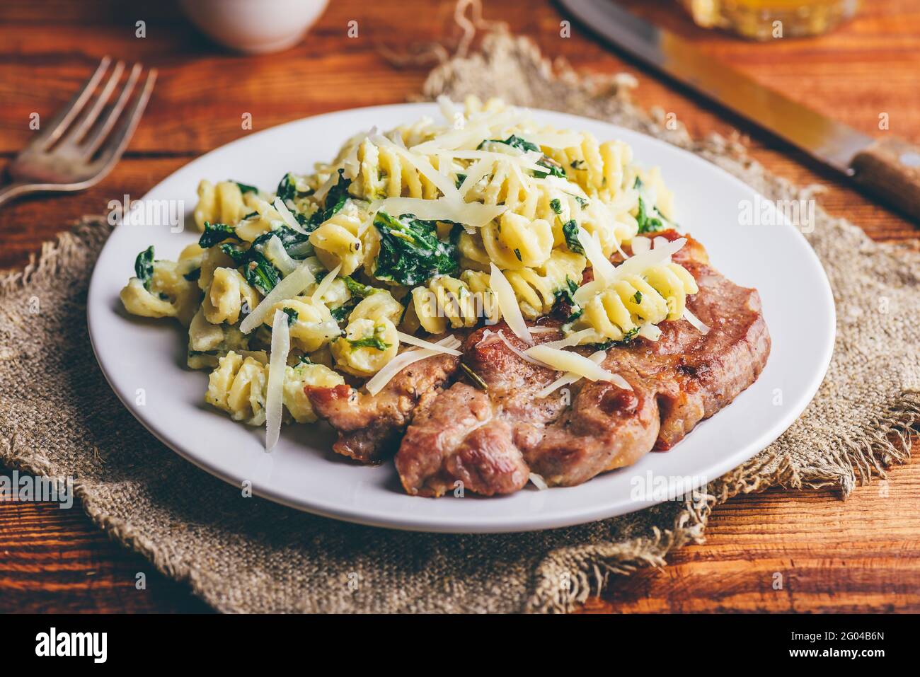 Bistecca di maiale e pasta cremosa di spinaci guarnita con parmigiano Sulla piastra bianca Foto Stock