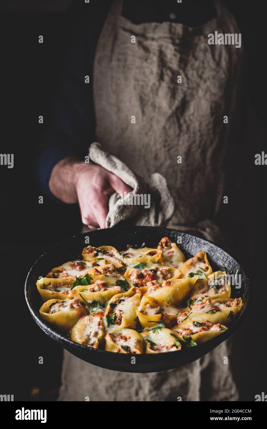 Lo chef conserva la padella di conchiglie di jumbo al forno ripieni di manzo macinato, spinaci e formaggio Foto Stock