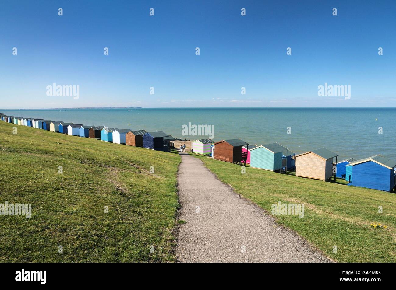 Una fila di colorate capanne sulla spiaggia lungo le rive erbose delle piste di Tankerton che si affacciano sulla spiaggia, appena fuori Whitstable, North Kent Coast, Inghilterra, Regno Unito Foto Stock