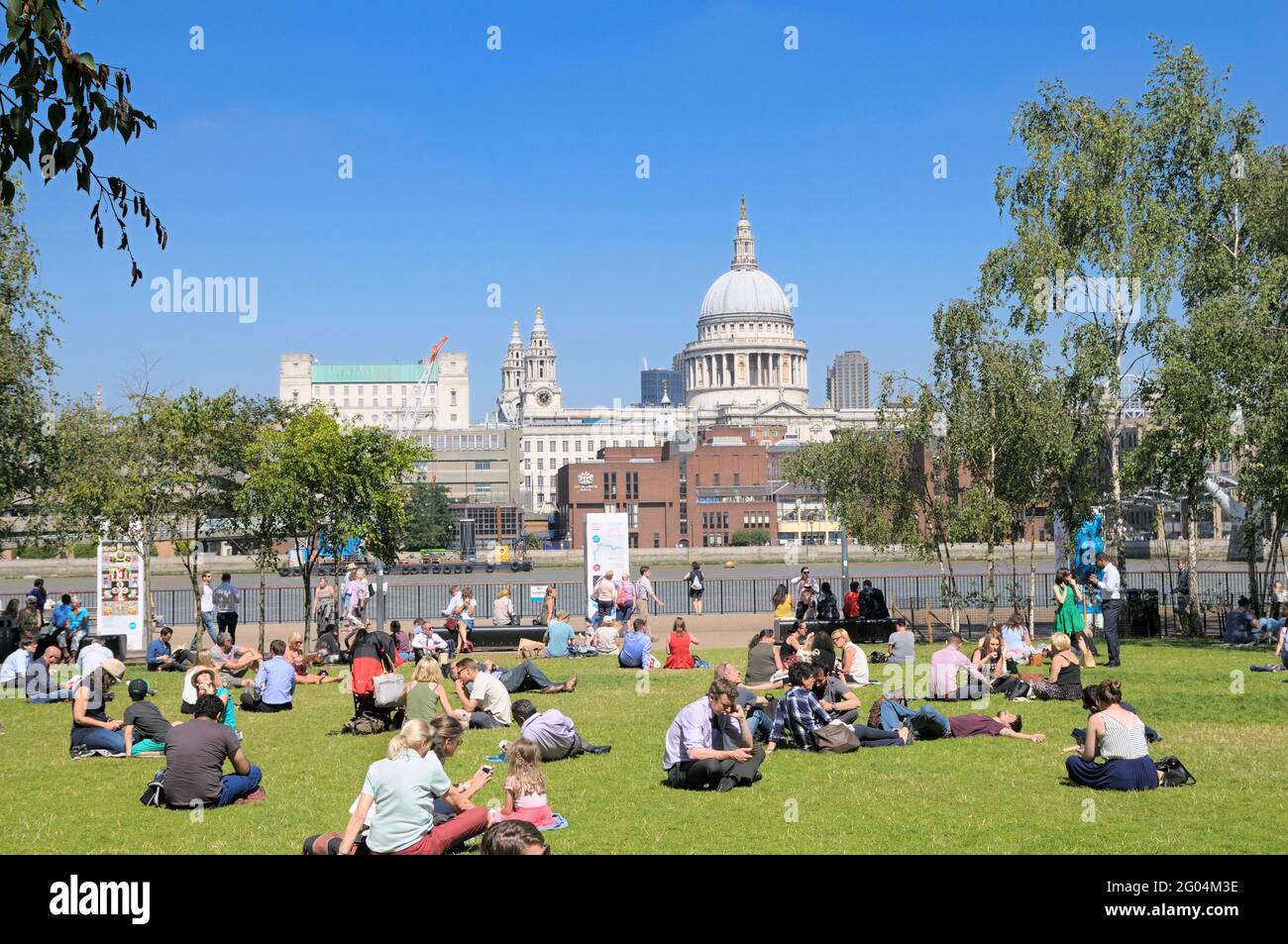 Persone che si rilassano sull'erba in una calda giornata di sole nei giardini Tate Modern di fronte alla Cattedrale di St Paul's, Bankside, South Bank, Londra, Inghilterra, REGNO UNITO Foto Stock