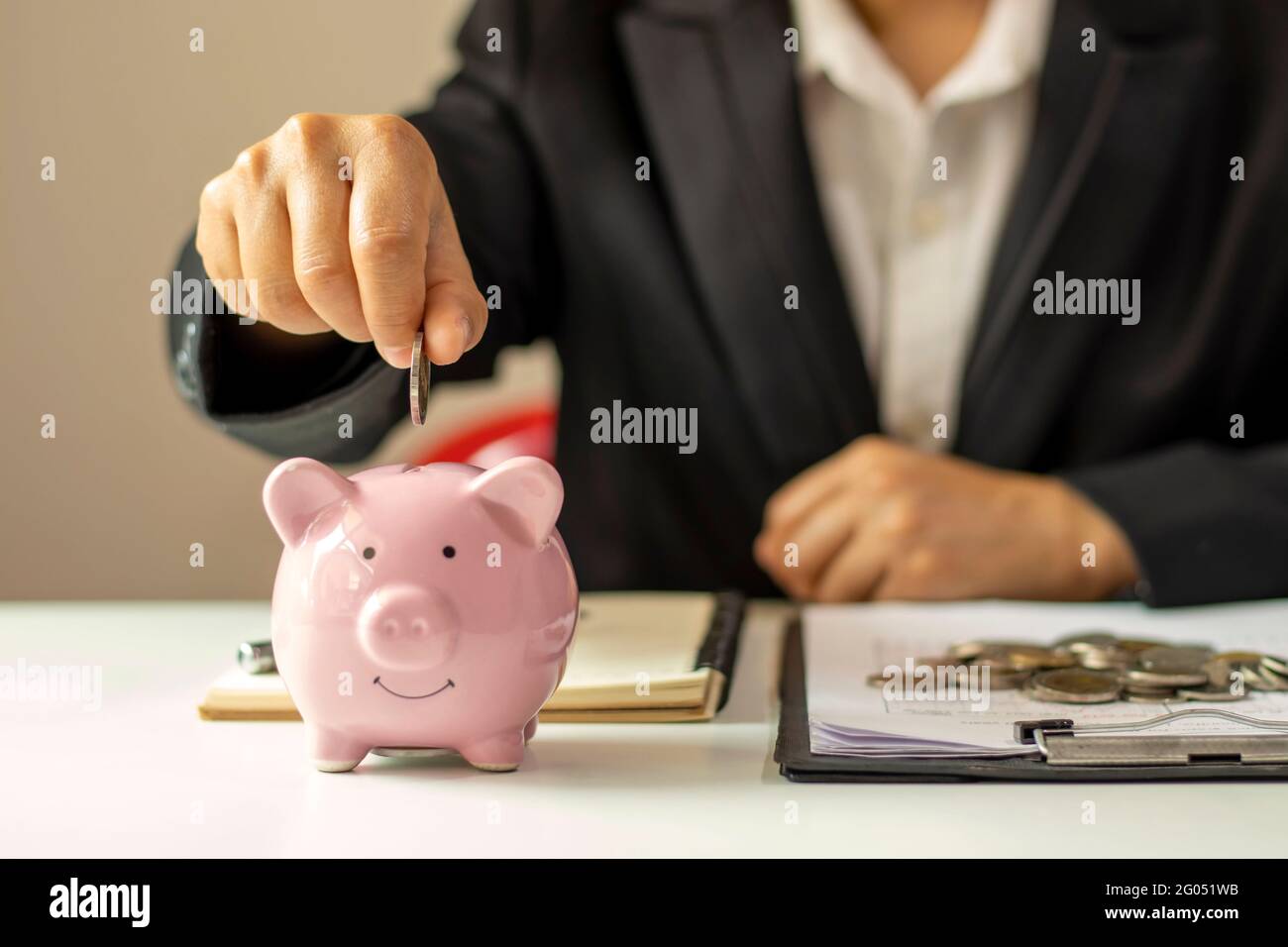 Primo piano di una donna d'affari che tiene una moneta in una banca piggy, un concetto di risparmio di denaro per la contabilità finanziaria. Foto Stock