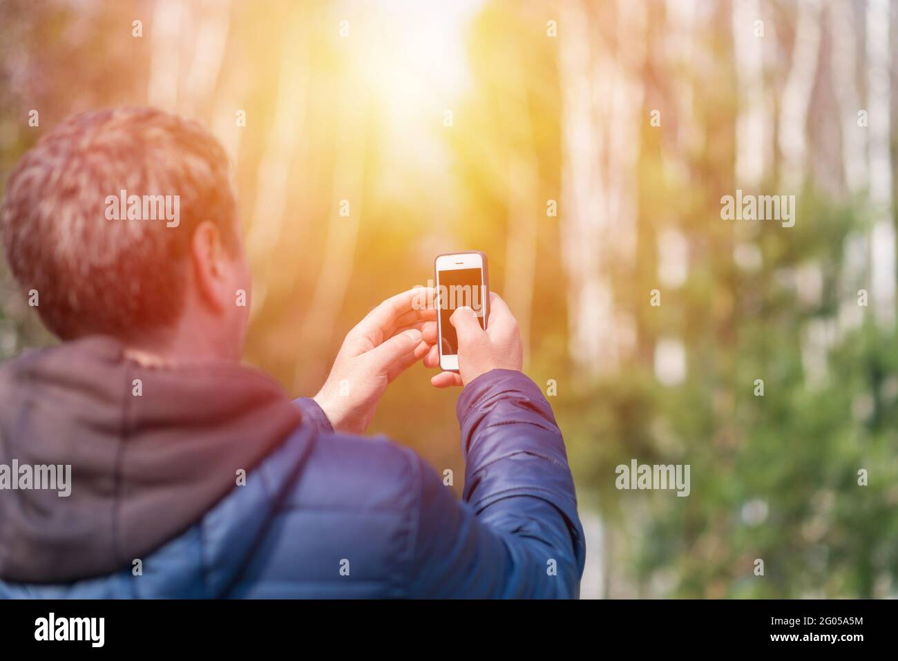 Un uomo di 40 anni con il suo smartphone cellulare alla ricerca del segnale di ricezione nella foresta primaverile soleggiata. Foto Stock