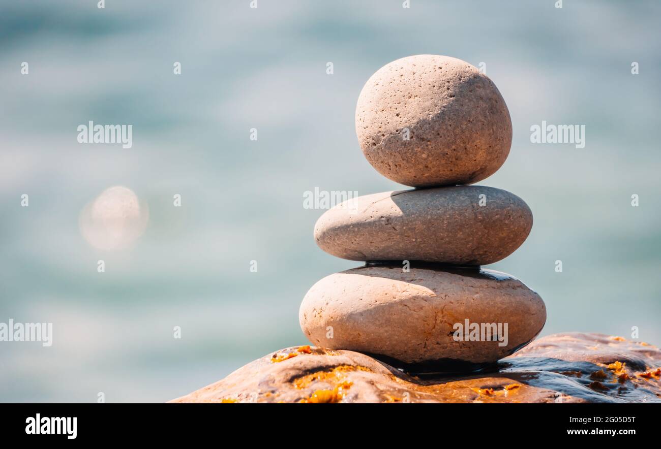 Equilibrata piramide di ciottoli sulla spiaggia in una giornata di sole. Abstract Sea bokeh sullo sfondo. Messa a fuoco selettiva. Pietre Zen sulla spiaggia di mare, meditazione Foto Stock