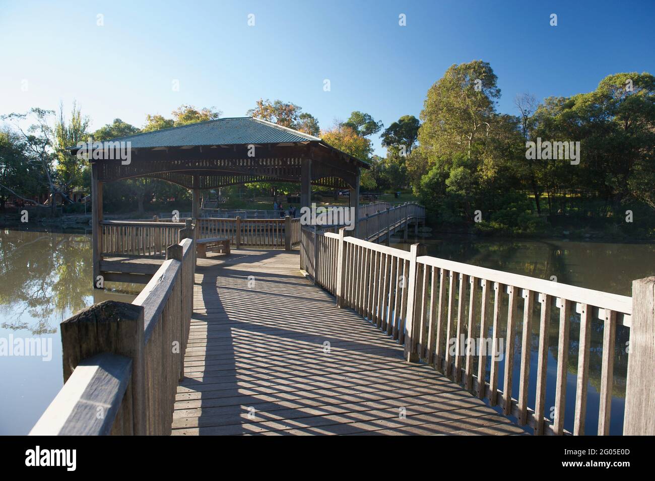 Il sole d'autunno crea motivi d'ombra sul ponte di legno che attraversa il lago Ringwood nella città di Maroondah a Victoria, Australia. Foto Stock