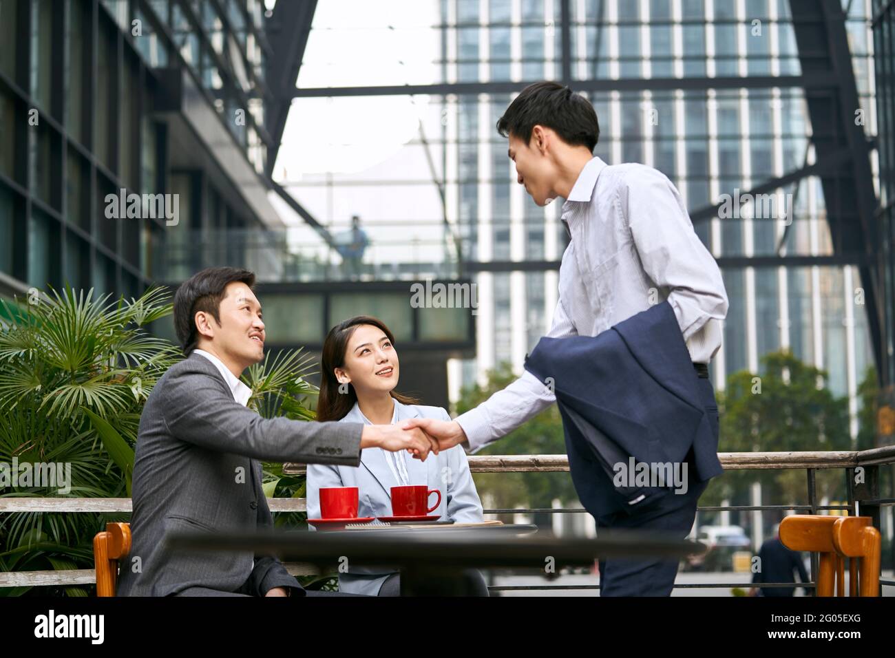 tre uomini d'affari asiatici che scuotono le mani incontrando in un outdoor caffetteria Foto Stock