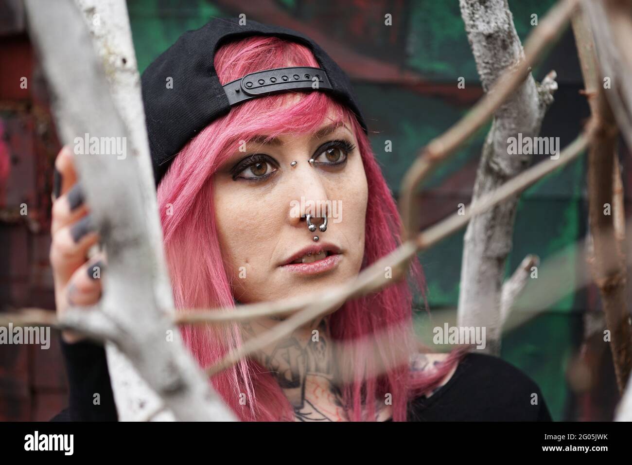 giovane donna con viso forato e collo tatuato dietro i rami dell'albero Foto Stock