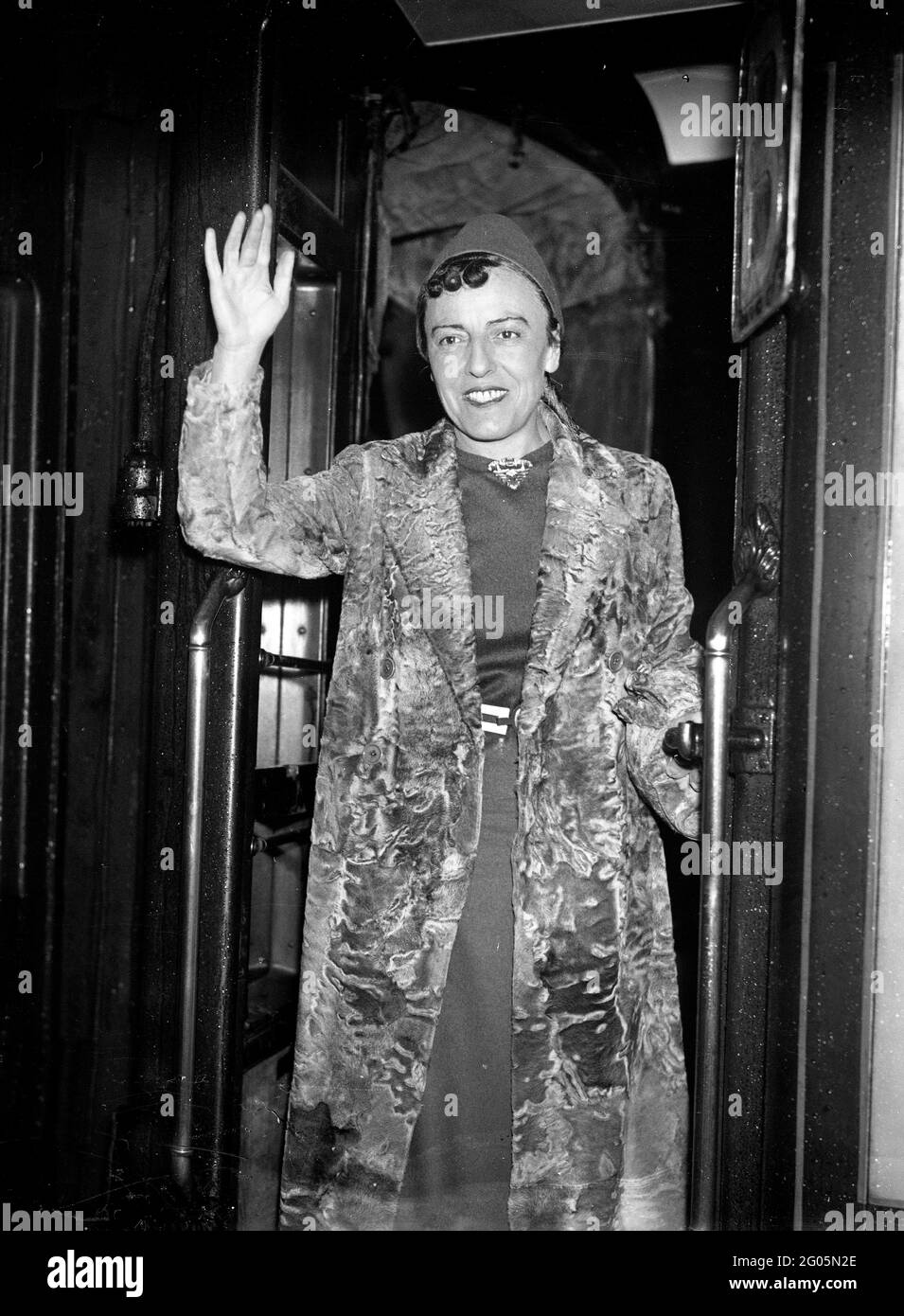Sali a bordo del treno 'RMS Queen Mary' per la sua prima visita alla romanziera e drammaturgo inglese Dodie Smith (1896 - 1990) che indossa il suo camice da pelliccia alla stazione di Waterloo, Londra, 27 ottobre 1937. Dorothy Gladys 'Dodie' Smith. Autore dei cento ed uno dalmati. Moda della pelliccia Gran Bretagna 1930 1937 donne donna donna donna donna autore scrittore Kiss curl Kiss ricci moda flamboyant dresser vestendo donna attrice donna donna sventolare femmina treno di cattura in partenza Foto Stock