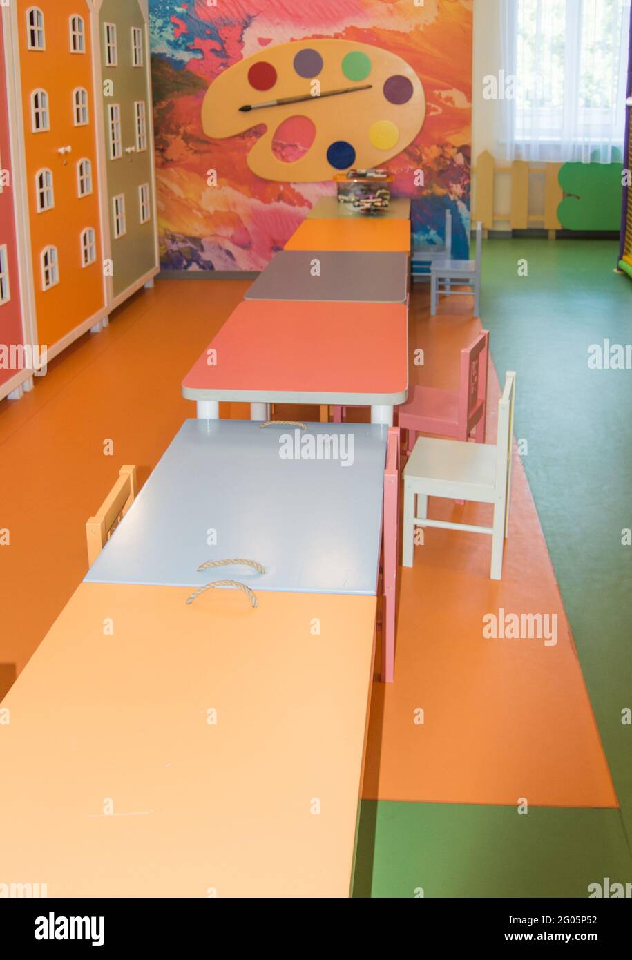 Moderna sala per bambini con tavoli in piedi in fila, un luogo per disegnare e giochi nella sala giochi dell'asilo. Foto Stock