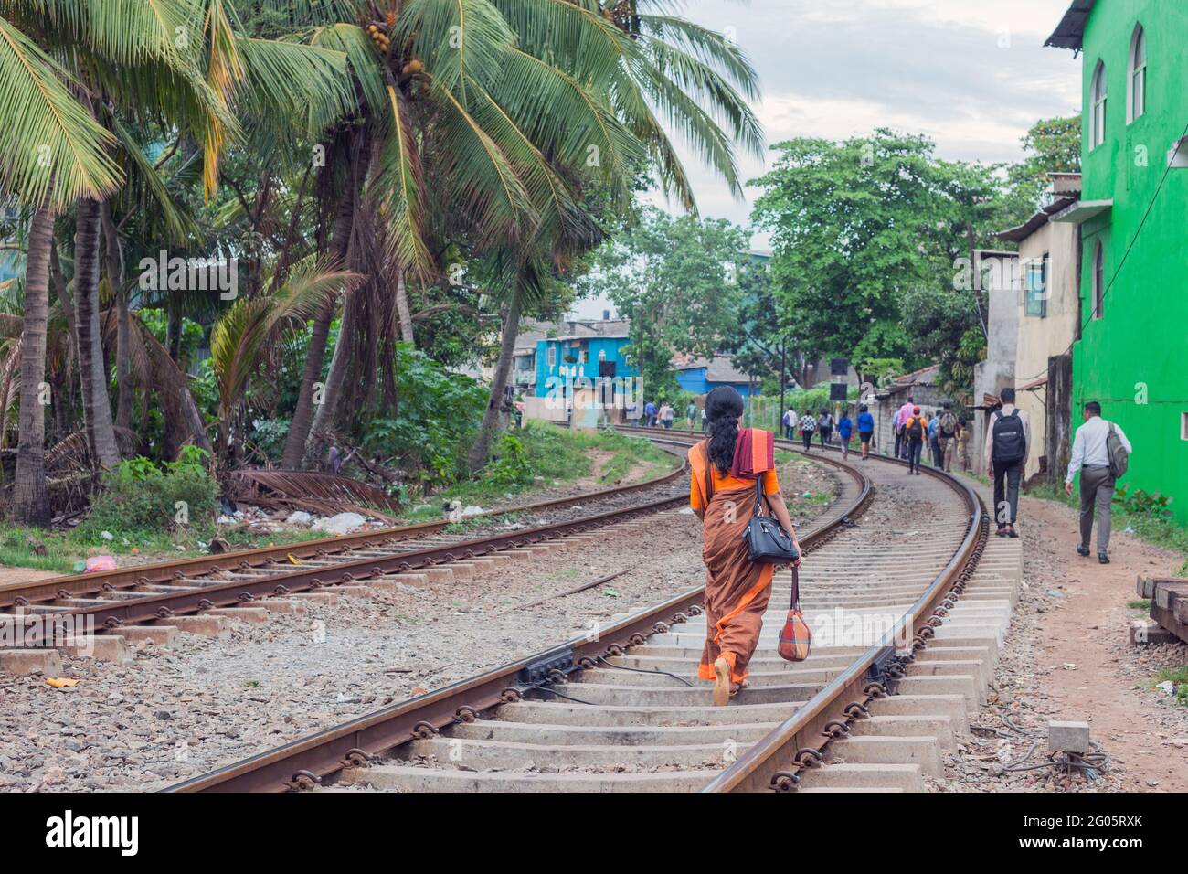 Sri Lanka femmina indossando sari arancio cammina lungo binari ferroviari verso la stazione ferroviaria dopo il lavoro, Colombo, Sri lanka Foto Stock