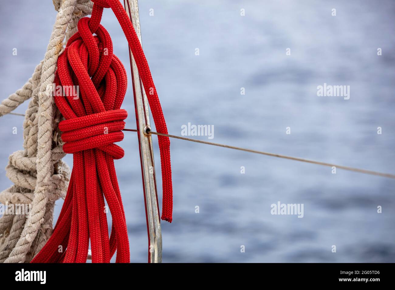 Corde di yacht sulla barca a vela, sfocare acqua di mare sfondo. Fune di  ormeggio di colore rosso sulla barriera di sicurezza in acciaio inox. Vista  di primo piano, spazio di copia.