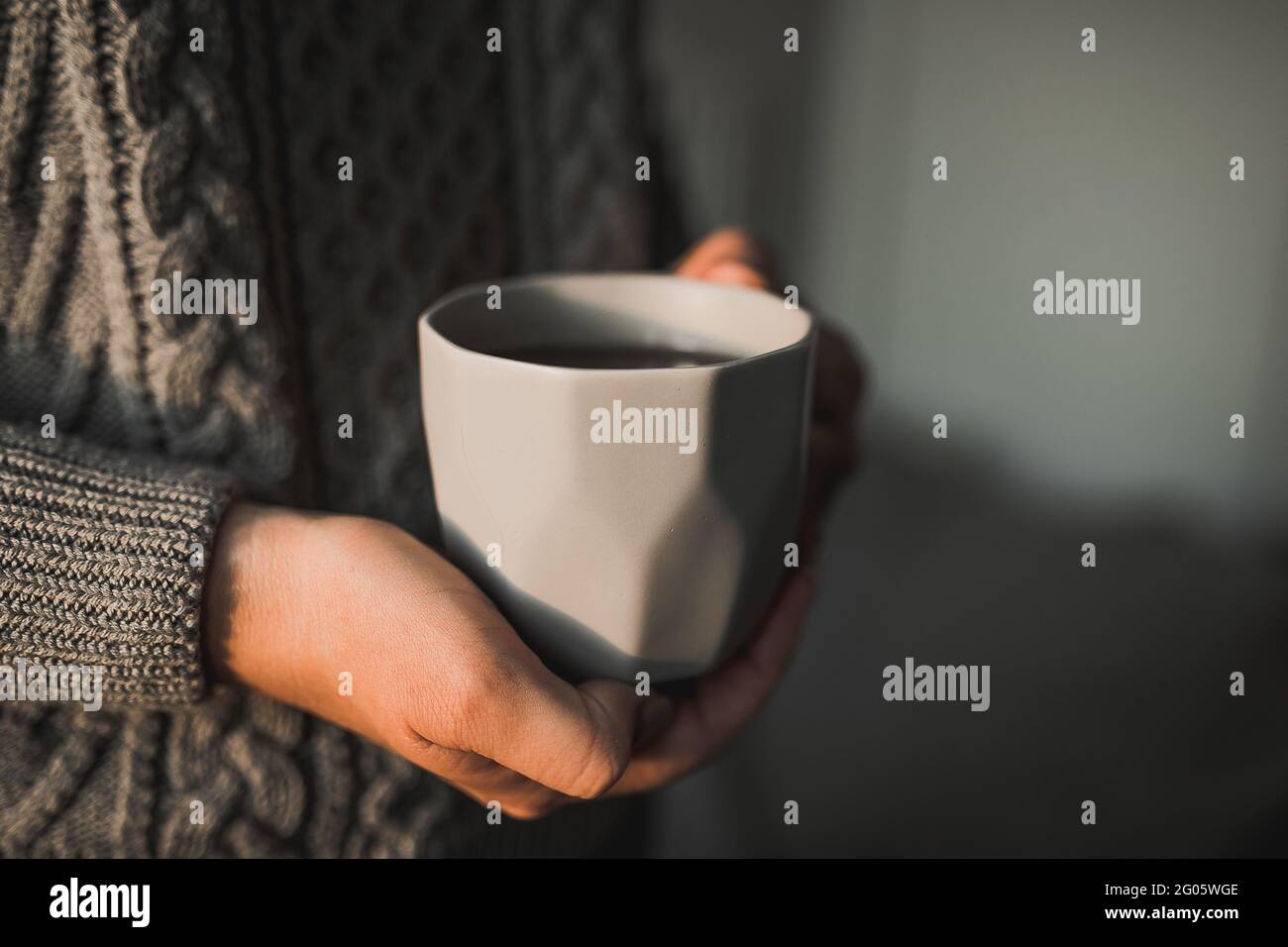 Donna in felpa a maglia grigia calda che tiene tazza di caffè, tè. Concetto di mattina invernale Foto Stock