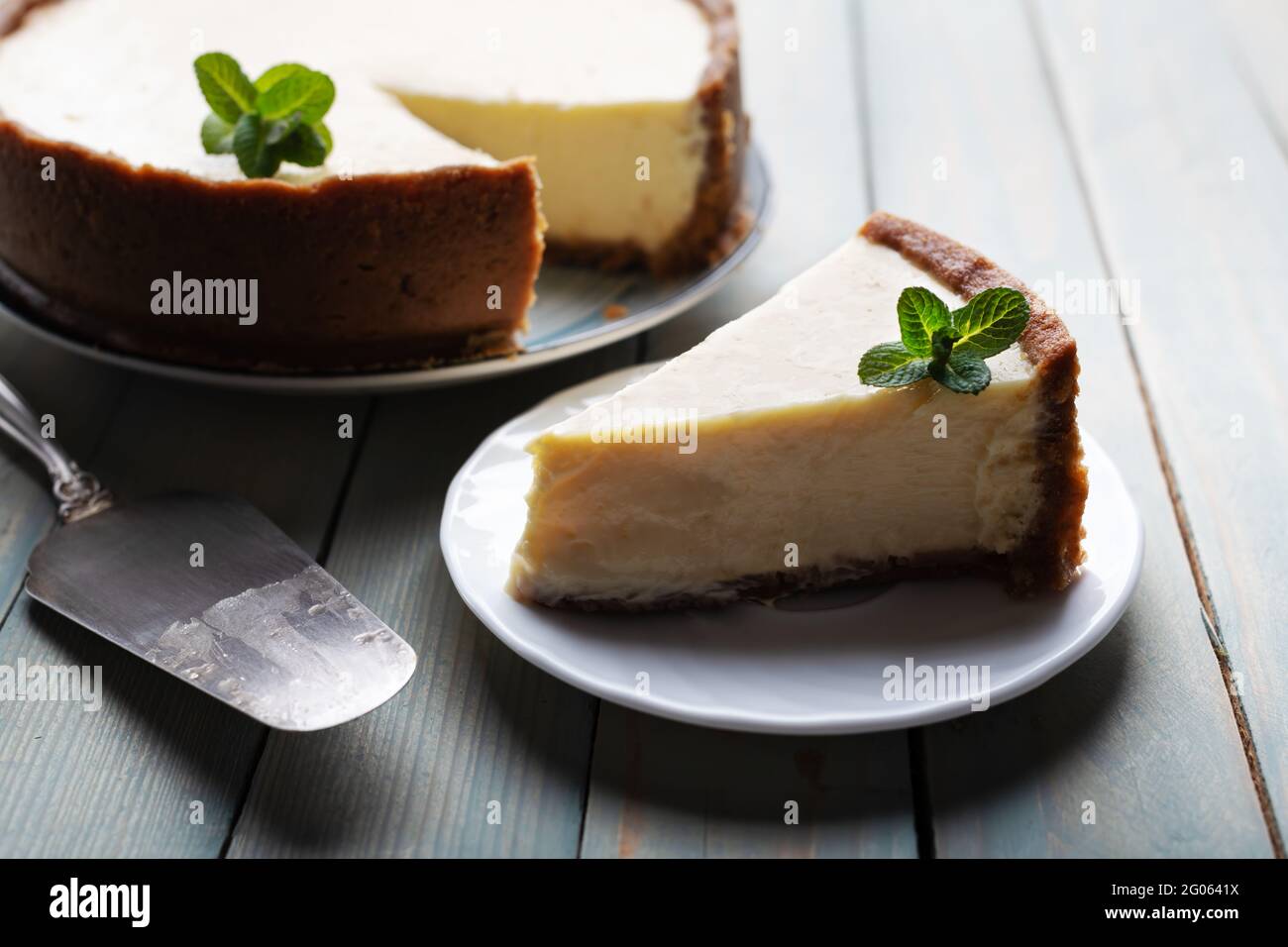 Aereo intorno alla classica cheesecake di New York e la sua fetta con rametto di menta su un piatto su un tavolo di legno. Il concetto di dolci e dolci dolci dessert Foto Stock