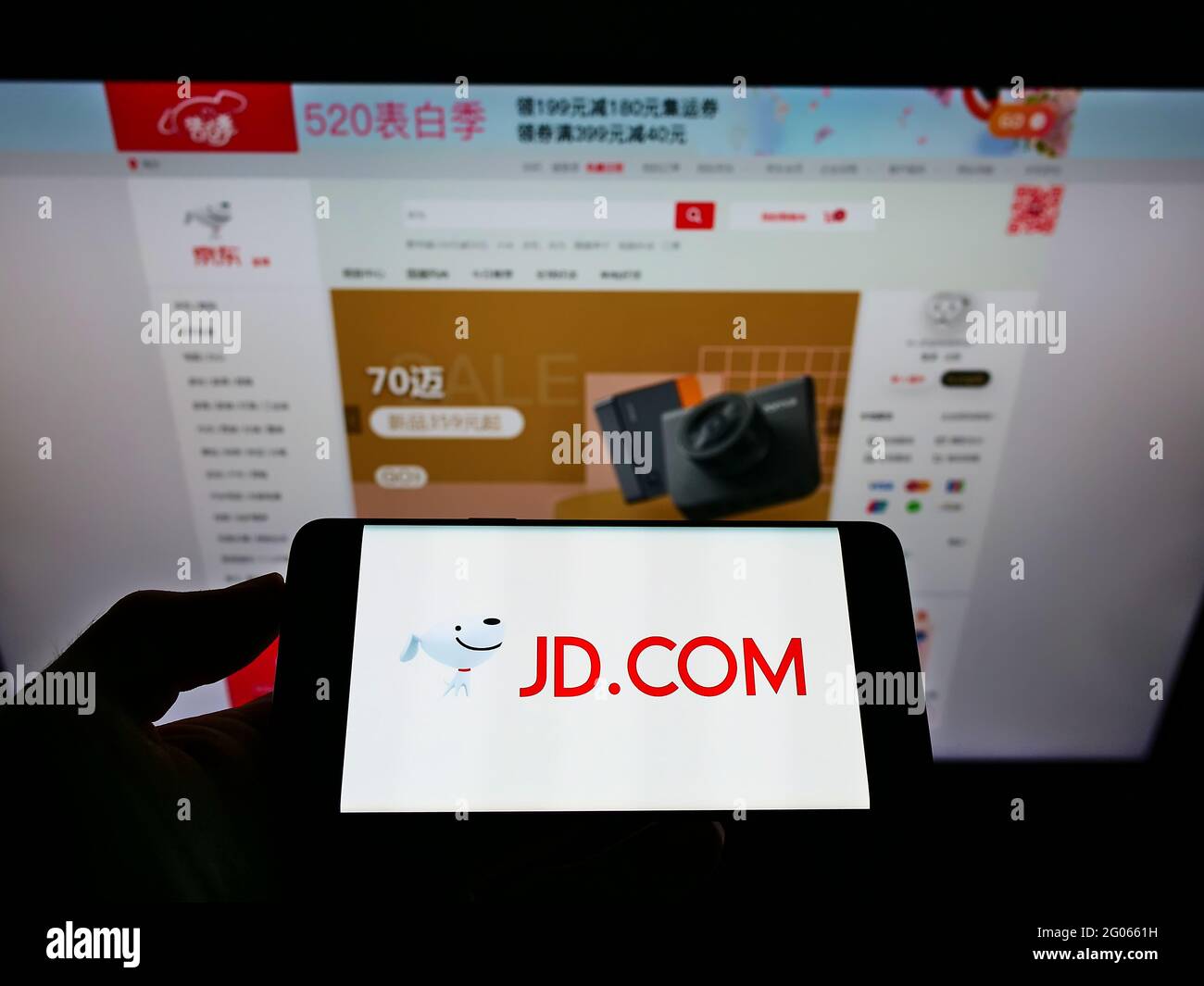 Persona che detiene smartphone con il logo della società cinese di e-commerce JD.com Inc. Sullo schermo di fronte al sito web. Mettere a fuoco il display del telefono. Foto Stock