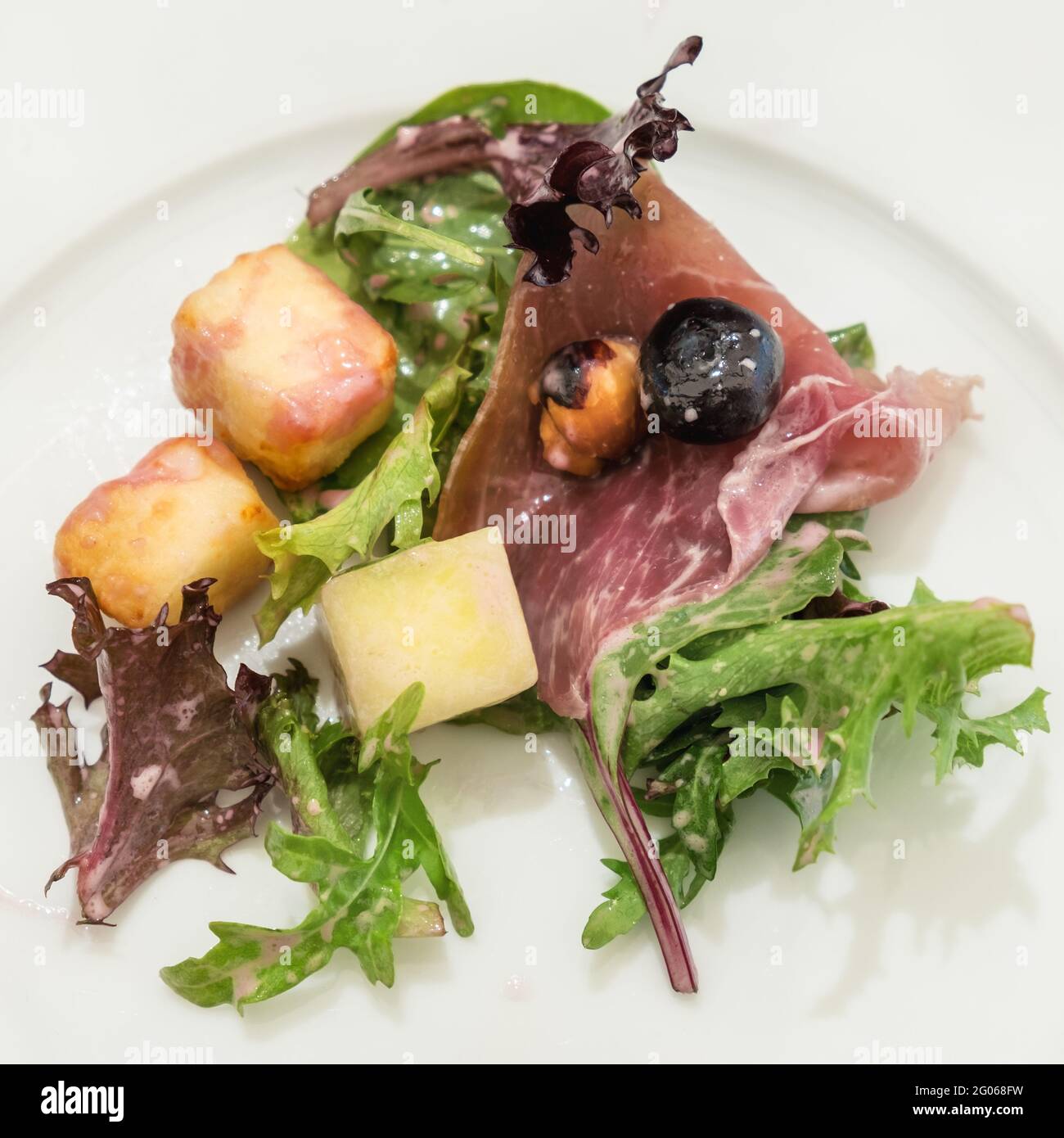 Piccola quantità di insalata con prosciutto, formaggio alloumi arrosto e insalata verde su piatto bianco. Foto Stock