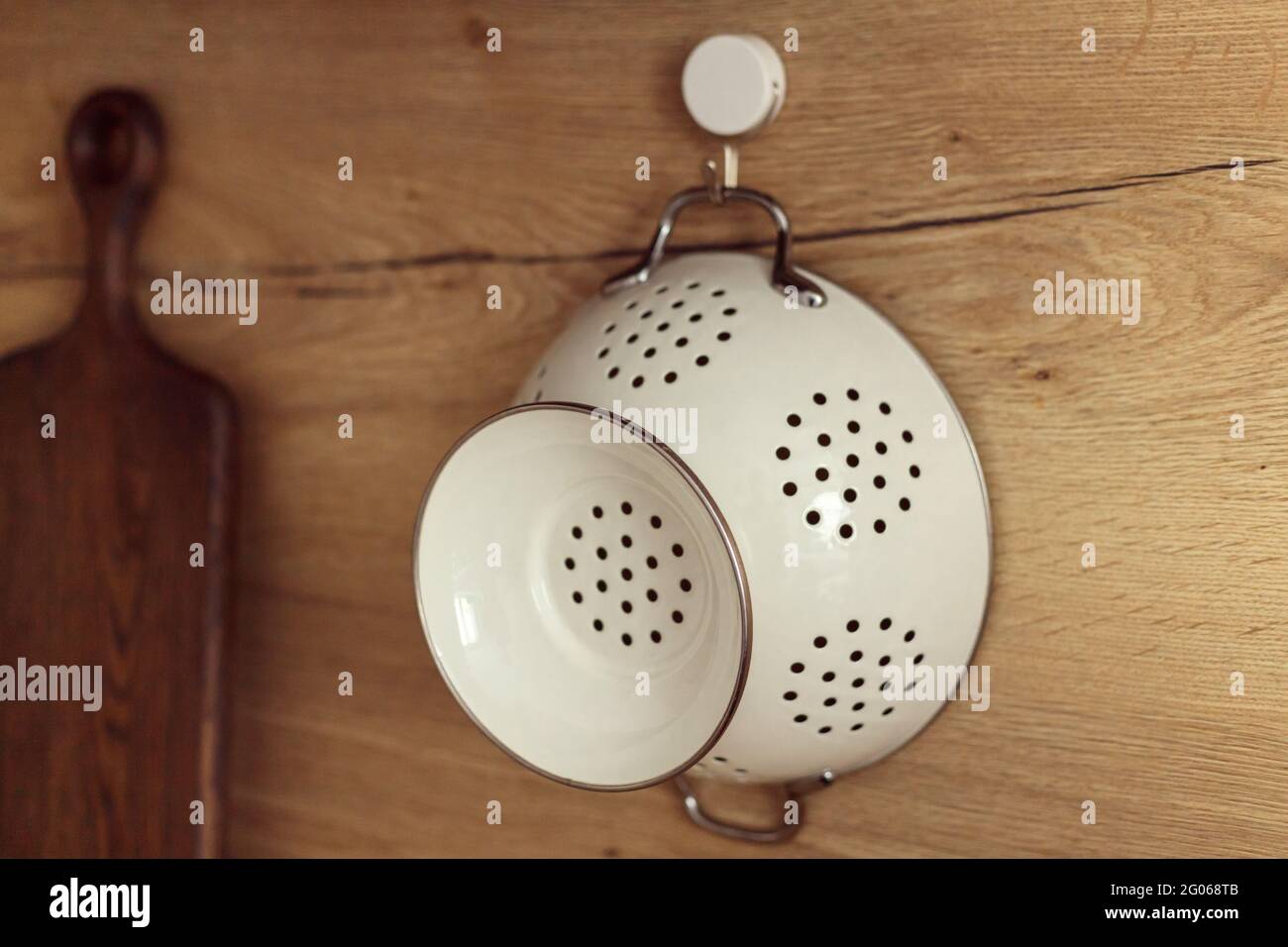 Il colander bianco di metallo appeso al gancio su una parete di legno della cucina. Foto Stock