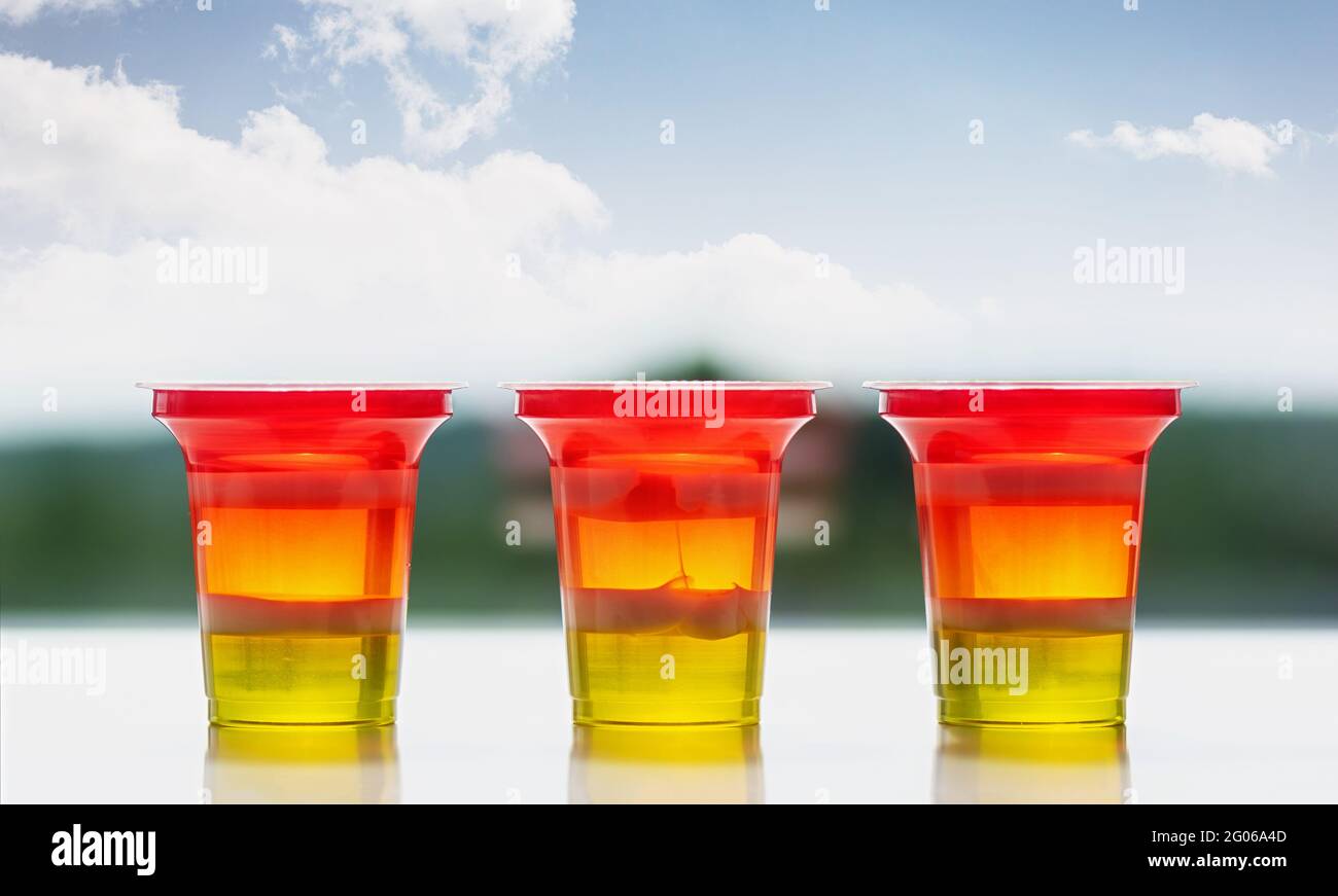 Tre bicchieri di gelatina a righe colorate su sfondo naturale. Gelatina arcobaleno per la festa dei bambini. Primo piano. Foto Stock
