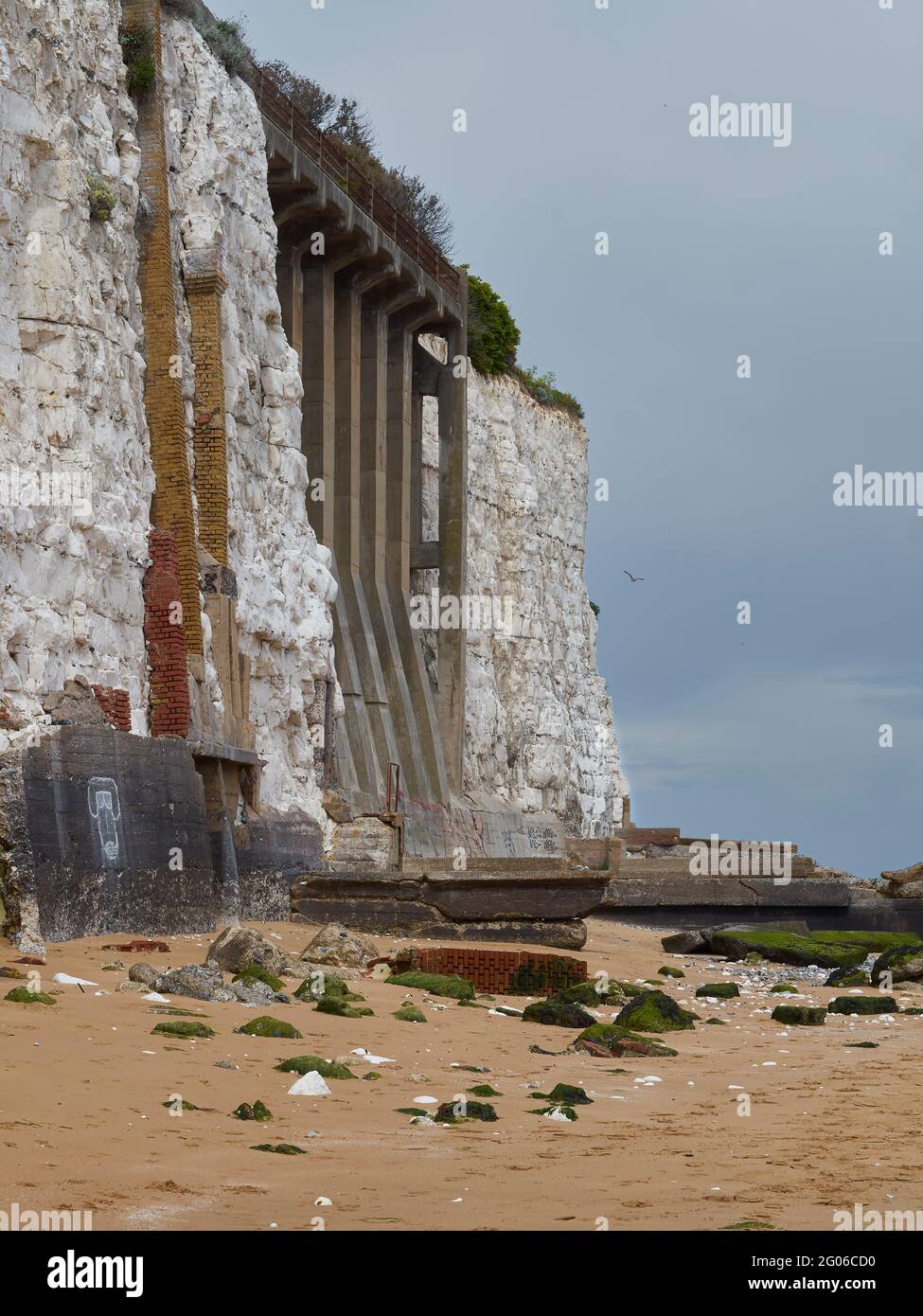 Imponenti sostegni per un passaggio pedonale e le difese costiere, adagiato su una scogliera di gesso a Stone Bay, con spiaggia di sabbia e cascata alla base. Foto Stock