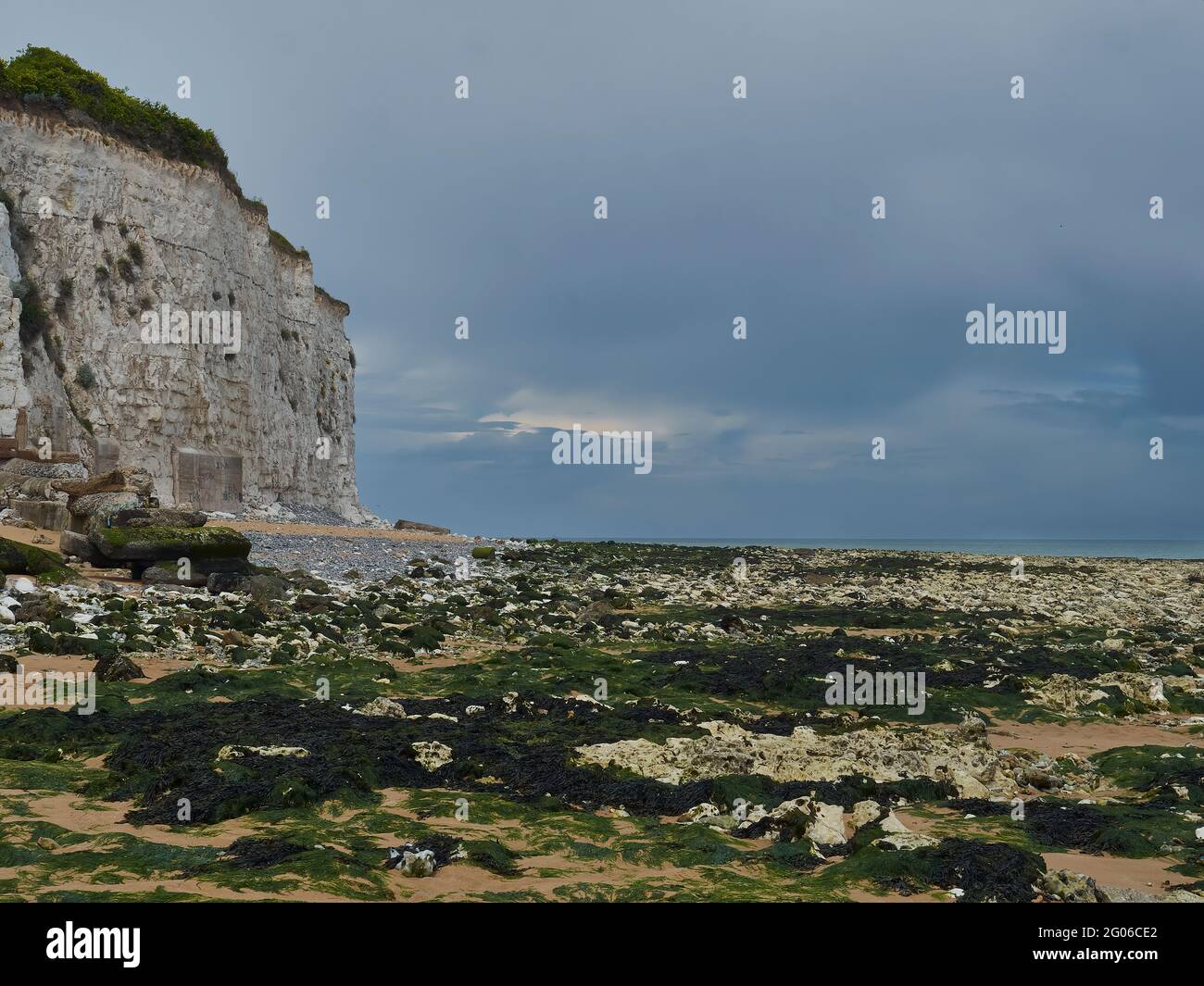 Un tratto desertizzato di spiaggia a Stone Bay, disseminato di cale rocciose dalla vicina scogliera di gesso. Un accenno di sole si rompe attraverso una nuvola lacerata in un cielo pesante. Foto Stock