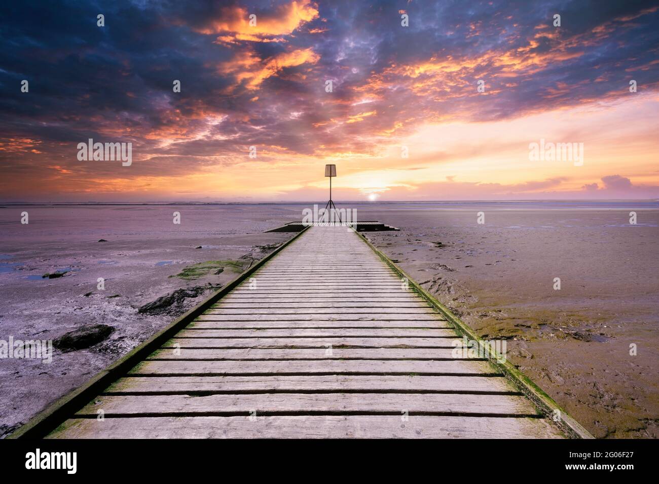 Le tavole di legno di un molo a Lytham in Lancashire, Regno Unito, si estendono sulla spiaggia di sabbia come il sole tramonta creando un cielo drammatico Foto Stock