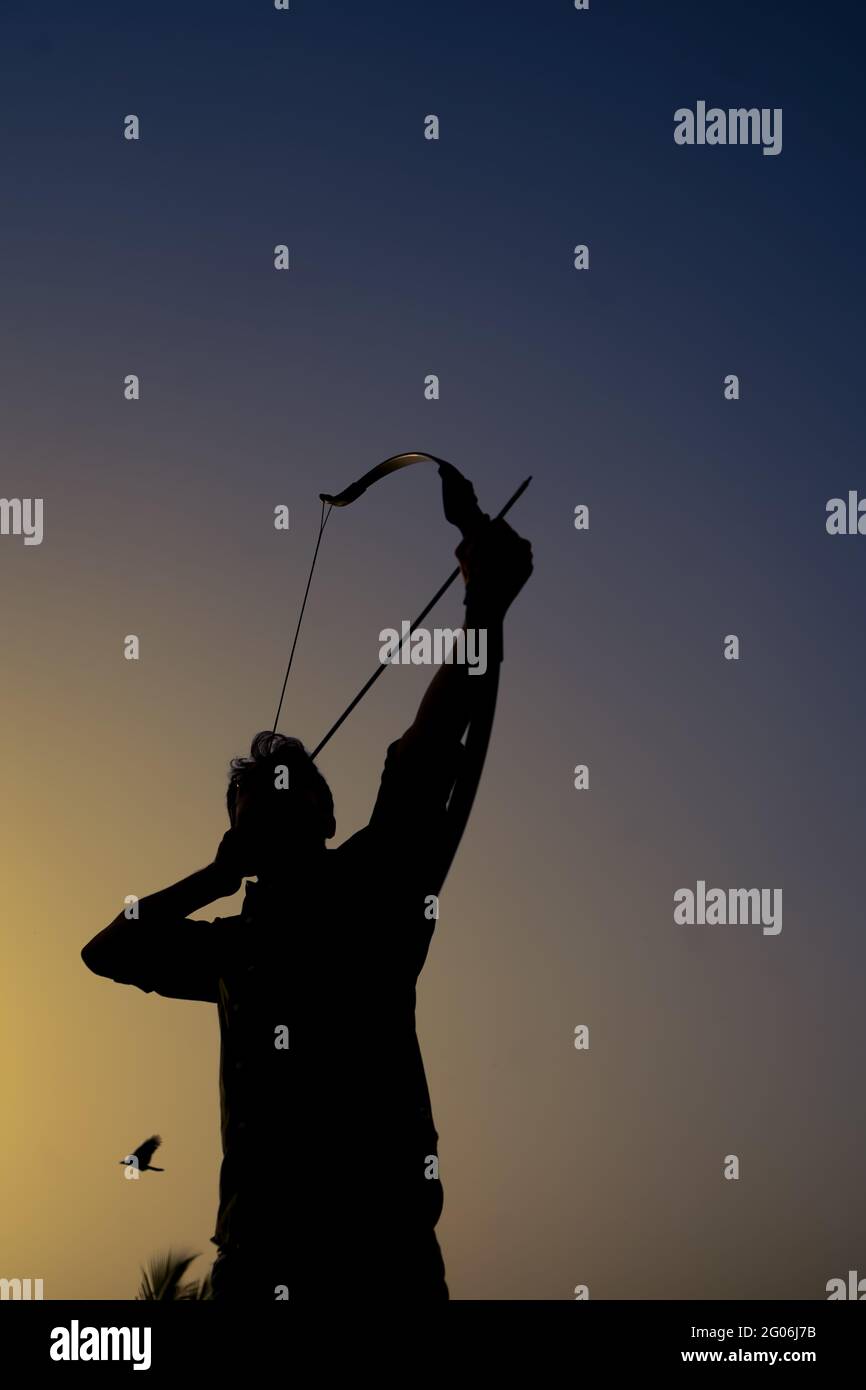 un uomo dalla silhouette che tiene un arco e una freccia davanti al tramonto. Foto Stock