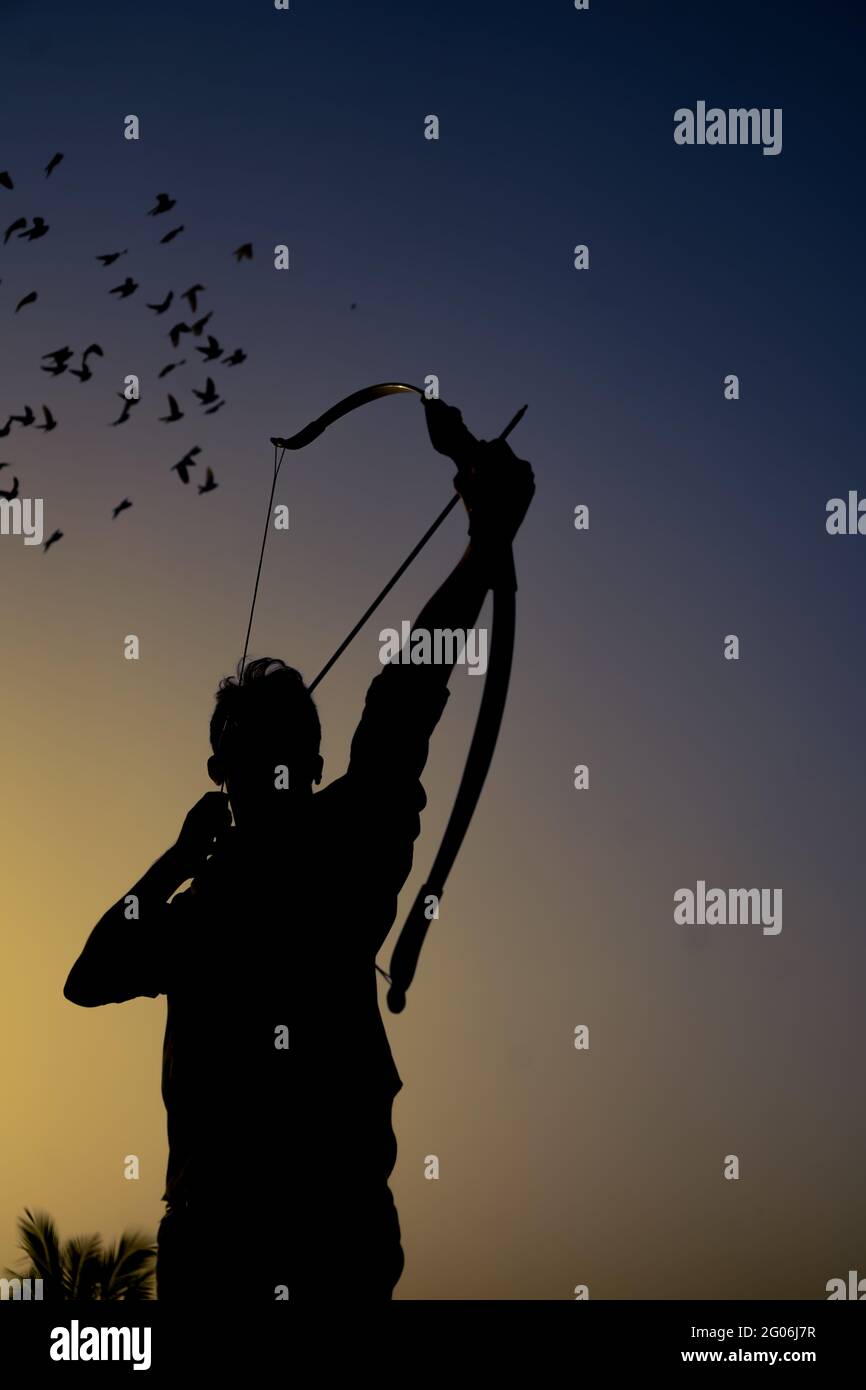 un uomo dalla silhouette che tiene un arco e una freccia davanti al tramonto. Foto Stock