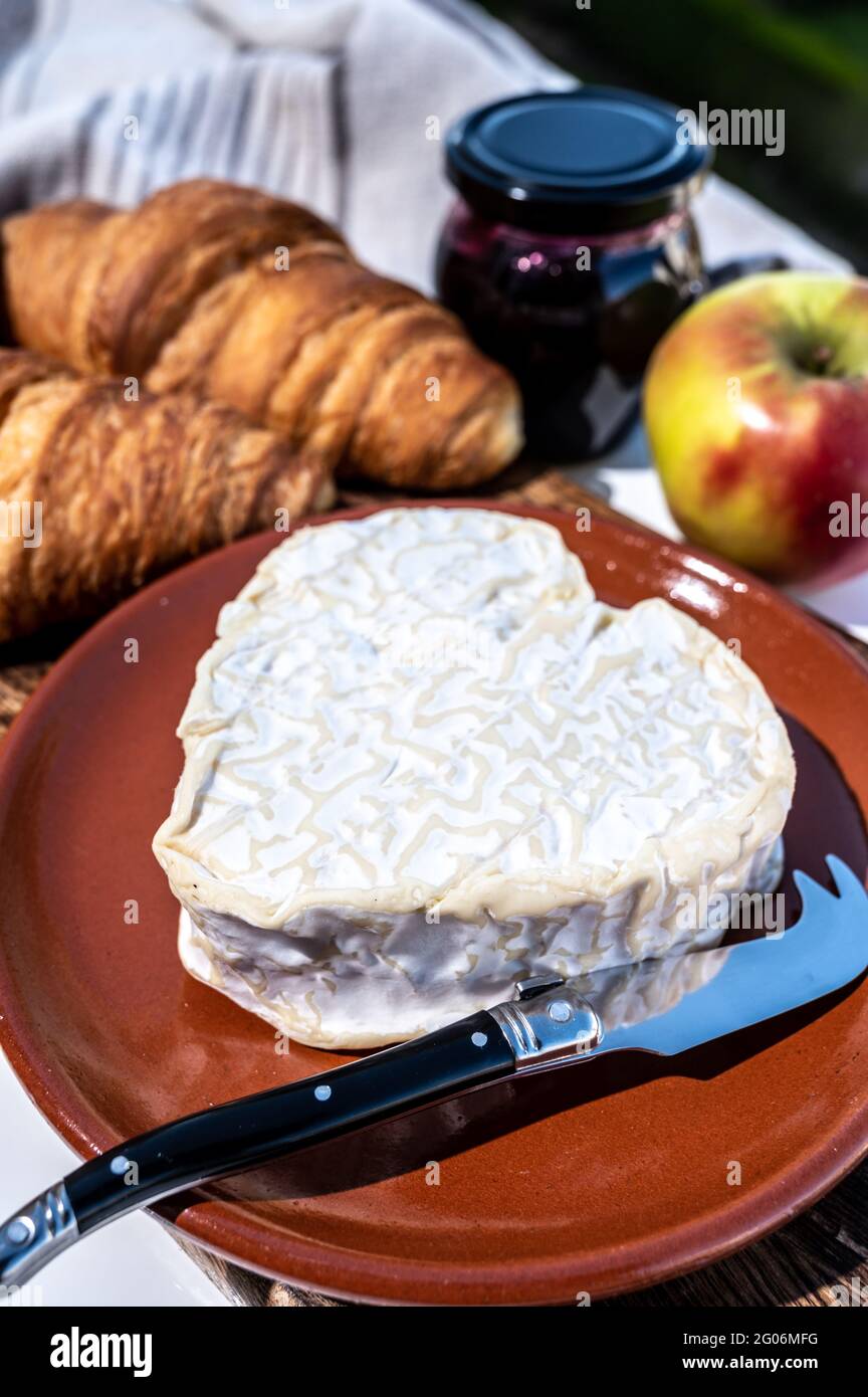 Colazione francese con croissant appena sfornati e formaggi della Normandia, neufchatel a forma di cuore servita all'aperto con bella vista sul villaggio francese Foto Stock