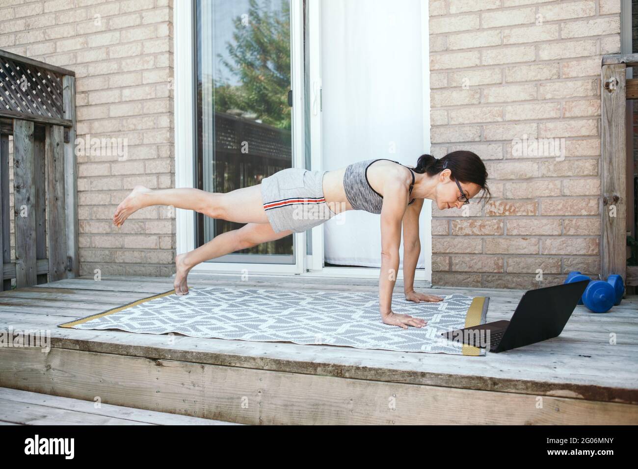 Donna caucasica di media età che fa esercizi di push-up sul cortile domestico online. Video fitness sport workout su Internet. Donna che impara in classe di formazione Foto Stock