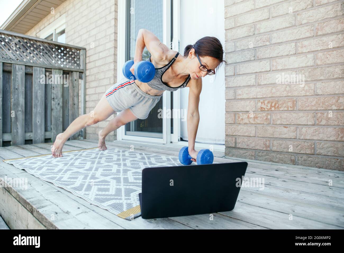 Donna caucasica di media età che fa esercizi di push-up con dumb-campane sul cortile domestico online. Video fitness sport workout su Internet. Donna che impara io Foto Stock