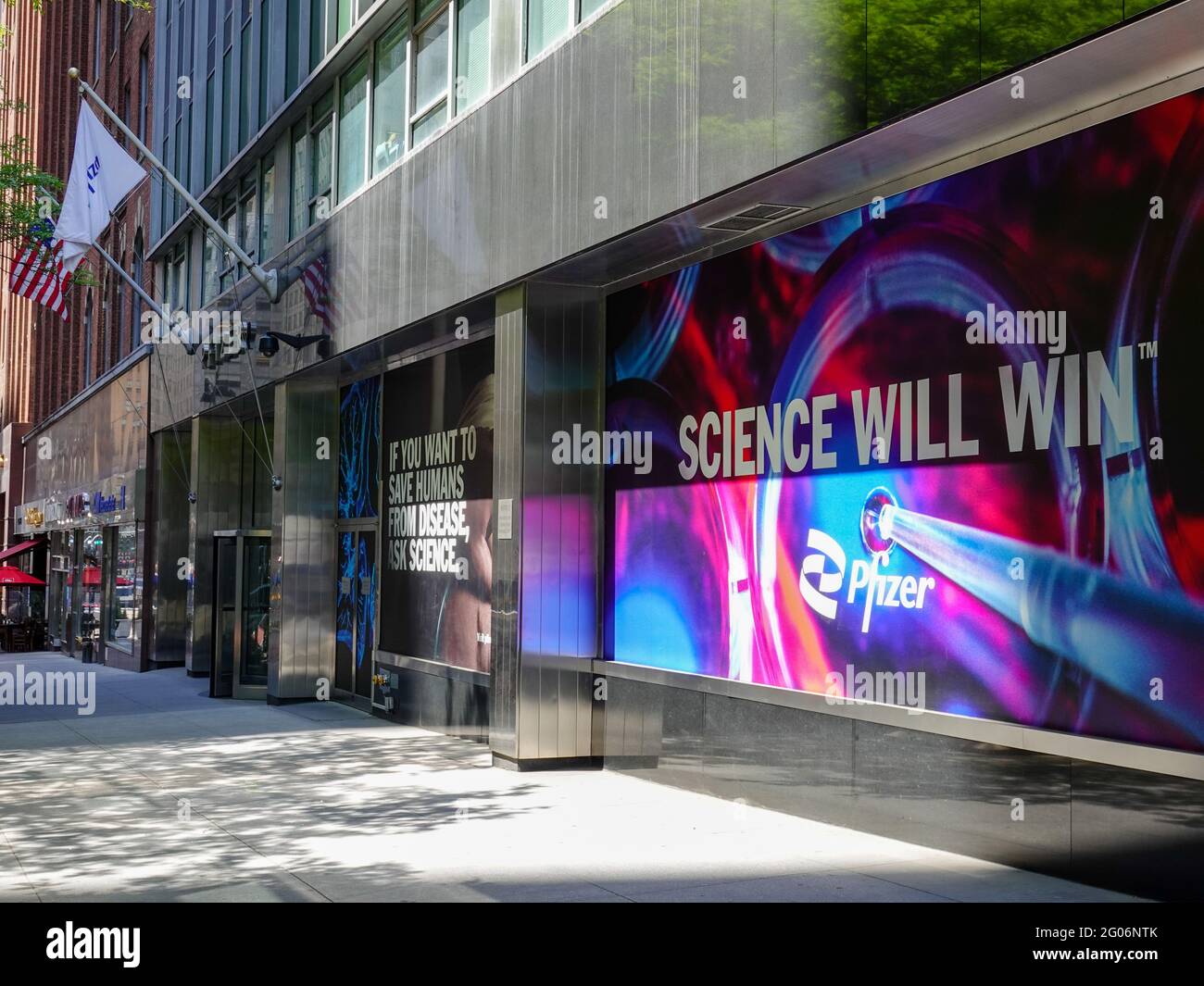 Lo slogan "Science Will Will Will Will Will Will Will" (la scienza vincerà) in vetrina degli uffici centrali di Pfizer World al 235 e 42nd Street, New York, NY, con la bandiera Pfizer con il marciapiede di NYC e i fronti dello shopping mentre gli Stati Uniti compiranno i progressi della vaccinazione. Foto Stock