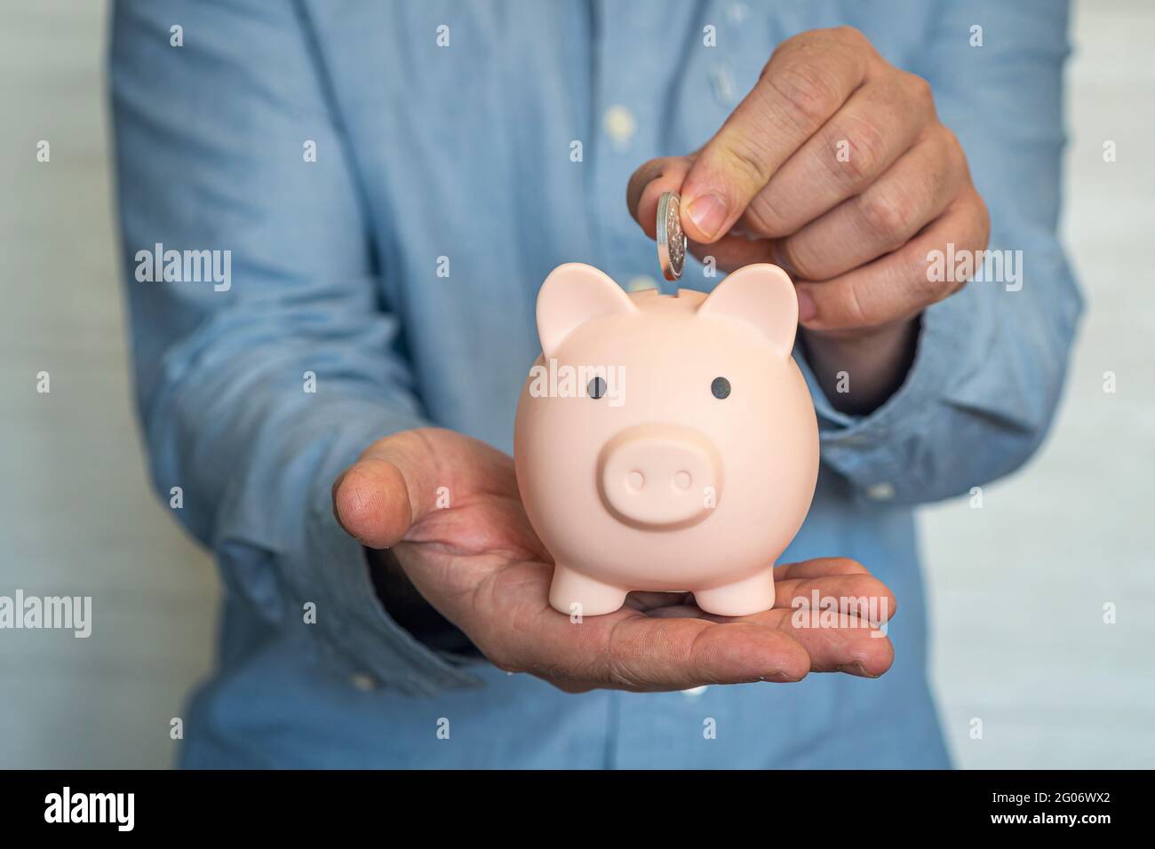 Uomo d'affari che mette la moneta in una piccola banca rosa piggy. Foto Stock