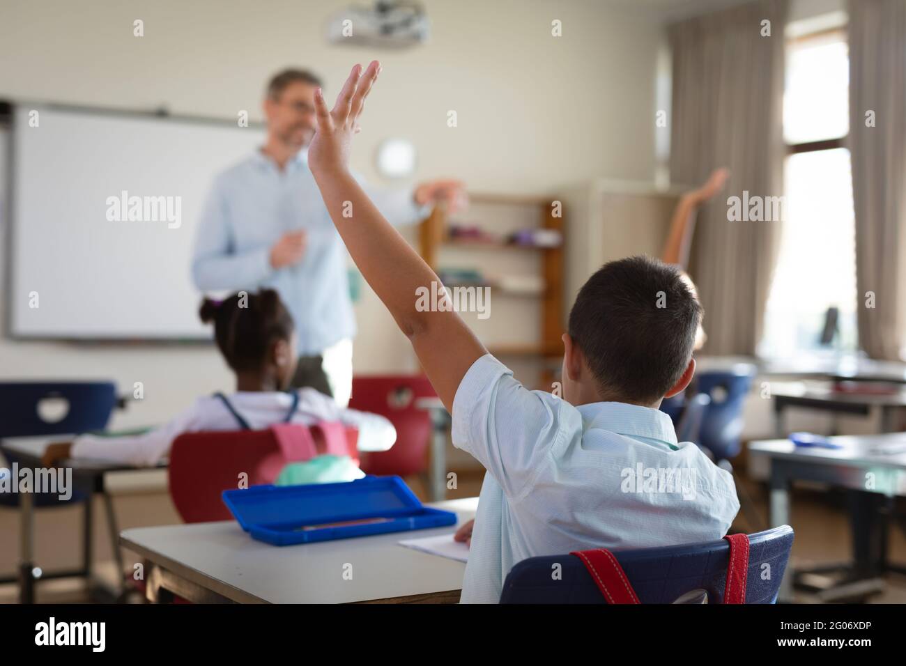 Gruppo di studenti diversi che alzano le mani nella classe delle scuole elementari Foto Stock