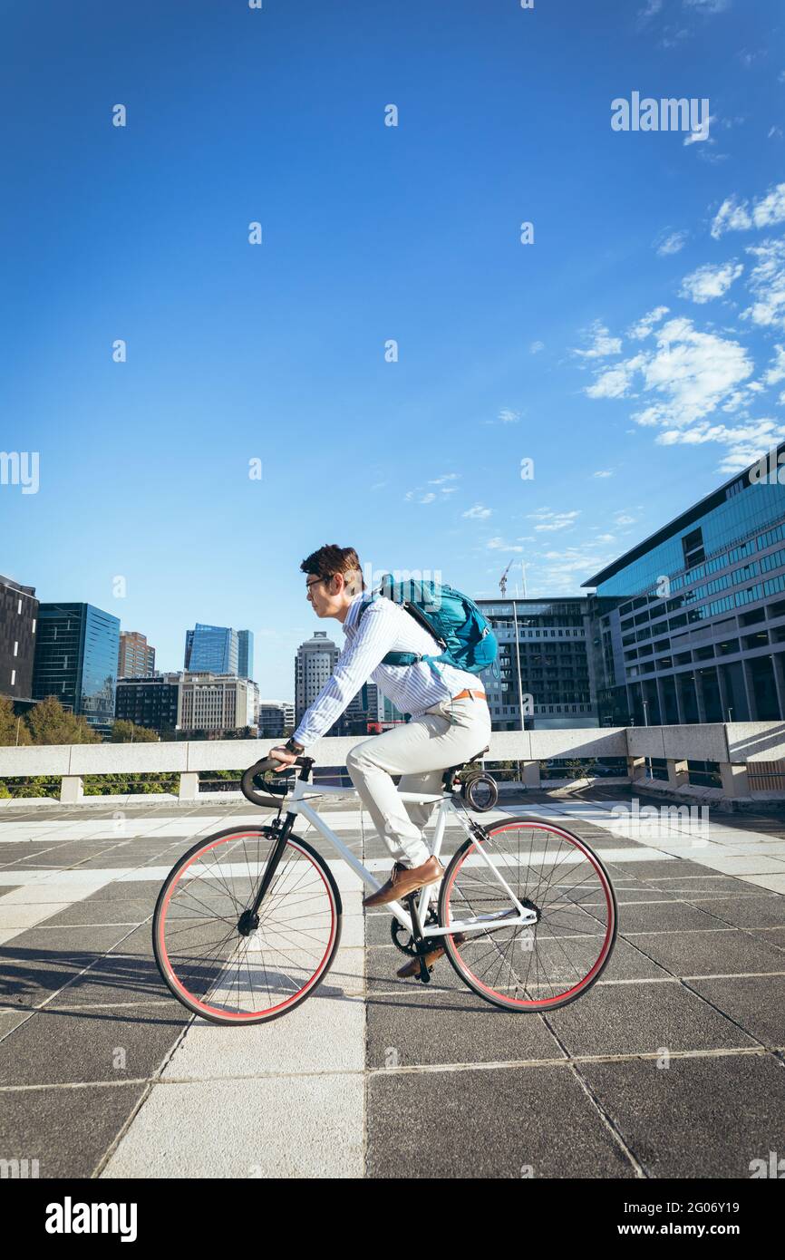 Uomo d'affari asiatico in bicicletta in strada con edifici moderni sullo sfondo Foto Stock