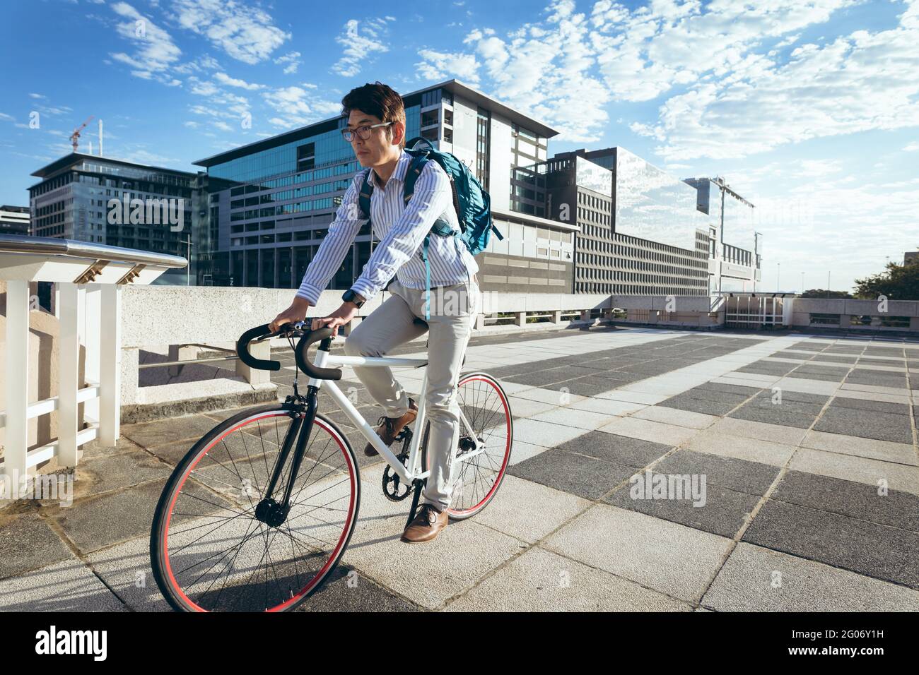 Uomo d'affari asiatico in bicicletta in strada con edifici moderni sullo sfondo Foto Stock