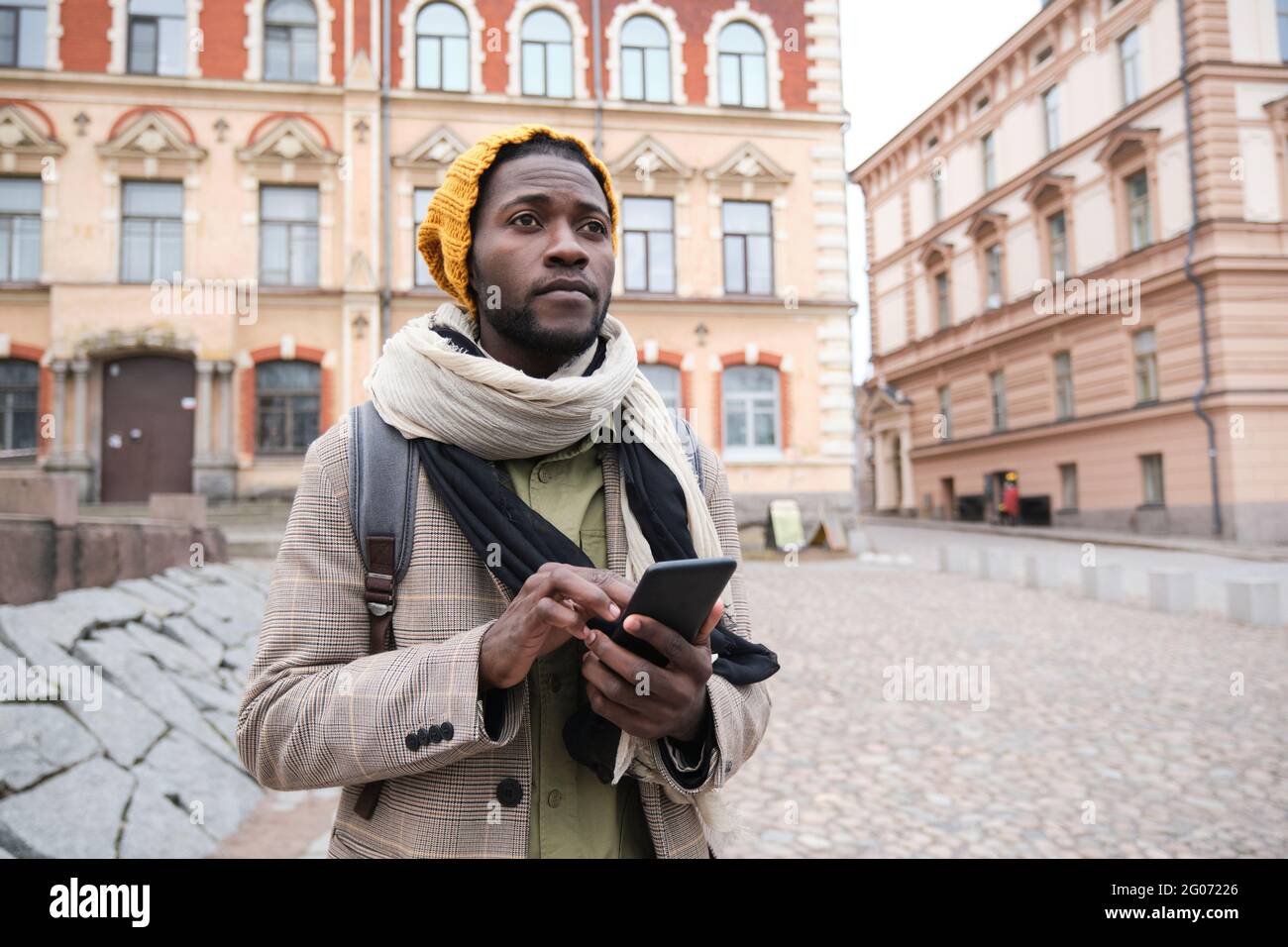 Uomo africano in abiti caldi utilizzando il telefono cellulare mentre si trova in città Foto Stock