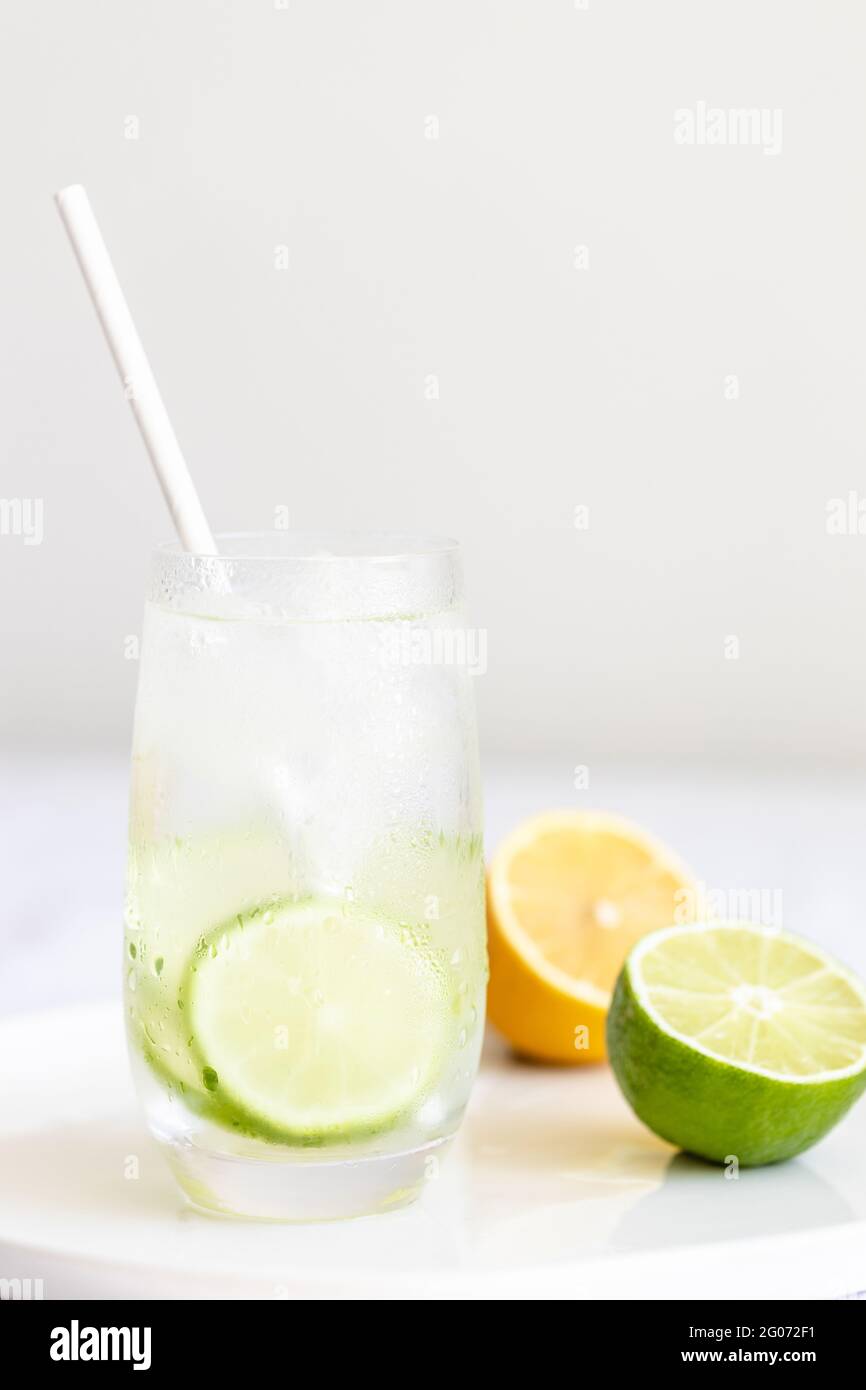Bicchiere di acqua di calce fredda con paglia di carta e halfs di lime e limone. Foto Stock